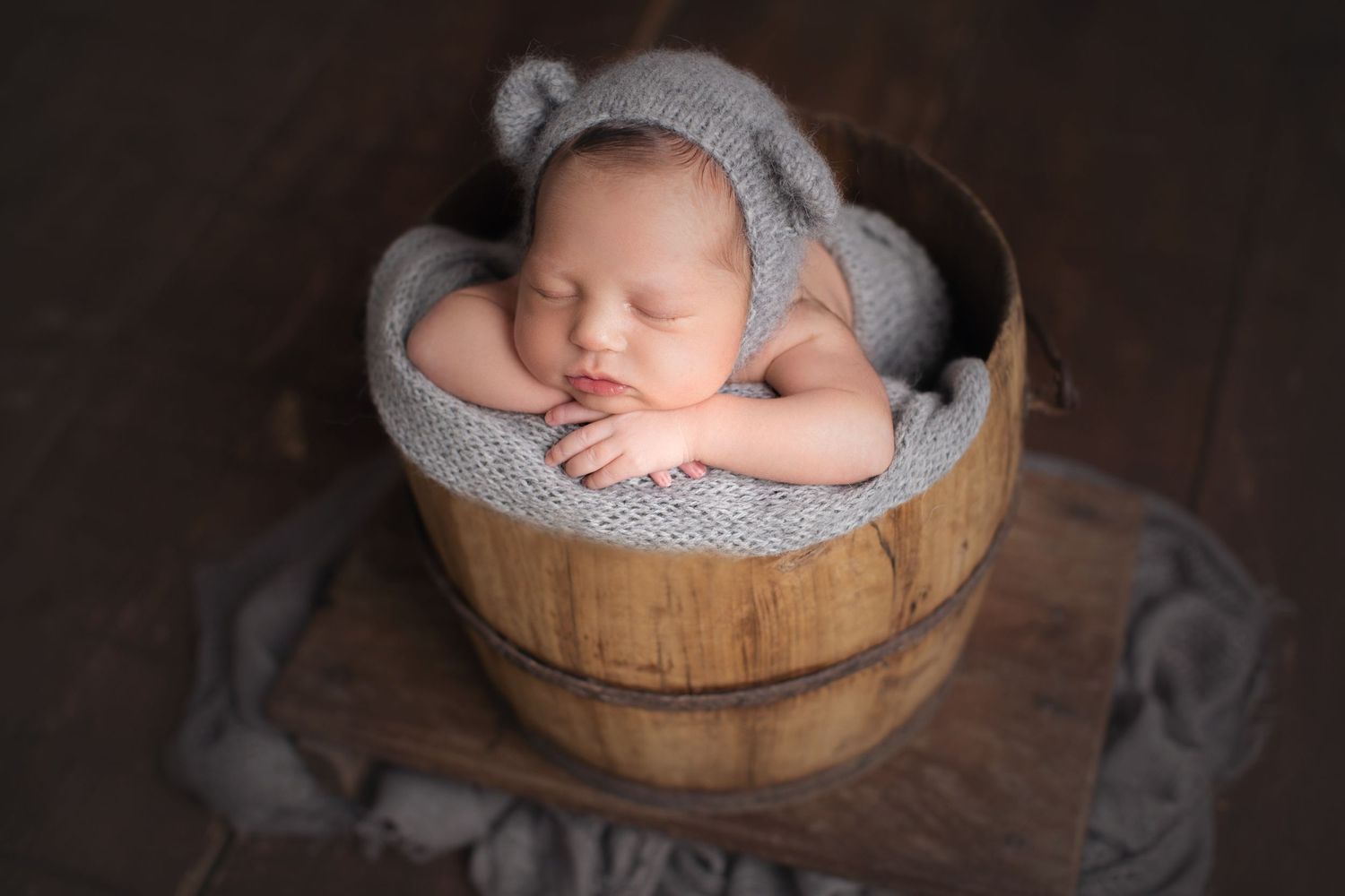 Sleeping newborn wearing gray bonnet in rustic wooden barrel. Dubai Photographer