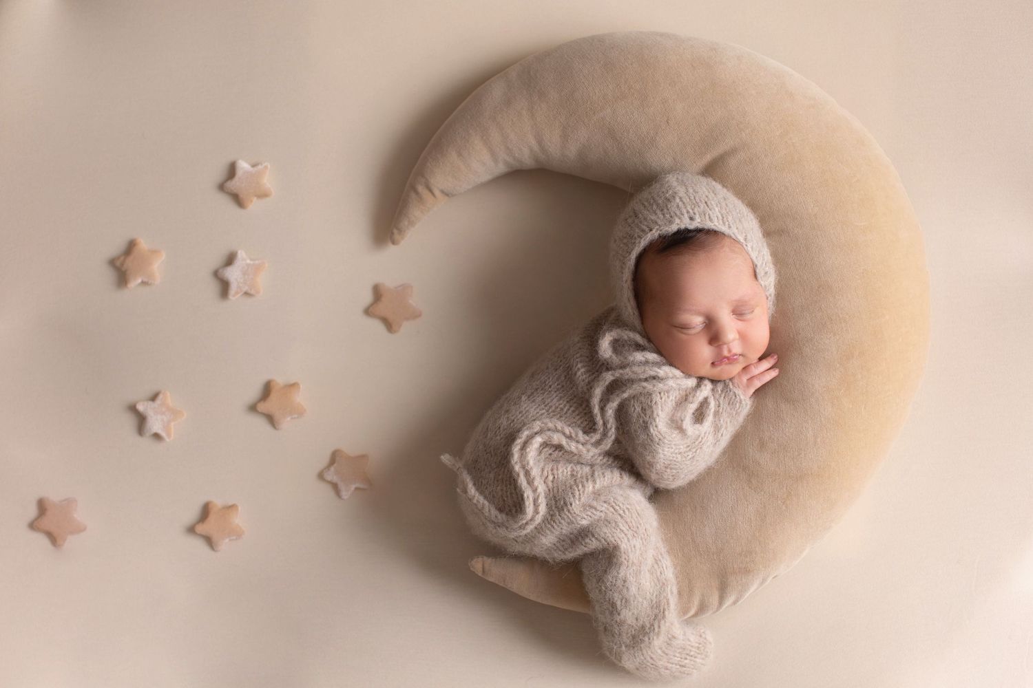 Newborn sleeping peacefully on a beige crescent moon prop with small star decorations. Dubai Photographer