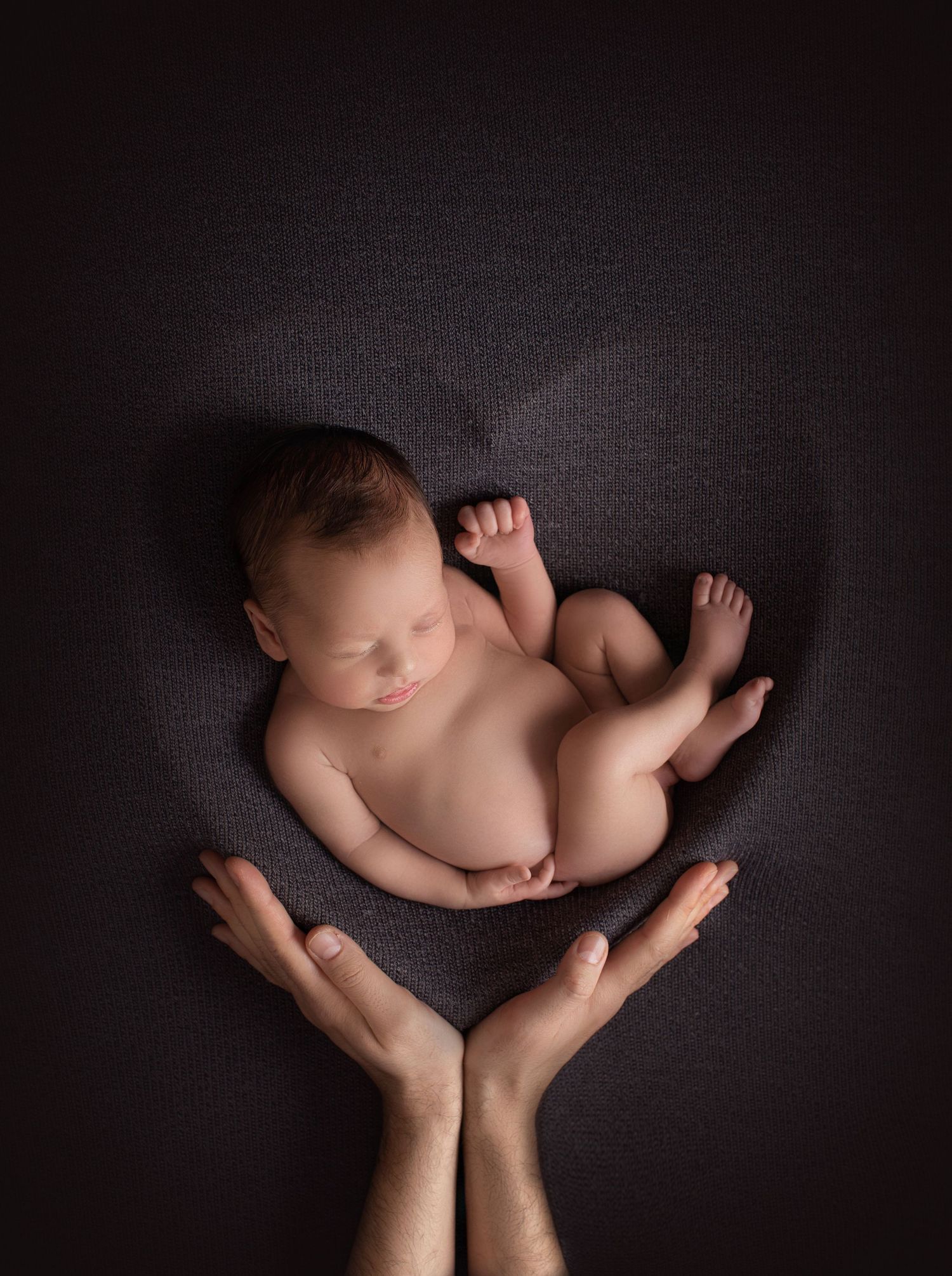 Artistic newborn photography with tiny baby cradled in hands against dark textured background. Dubai Photographer
