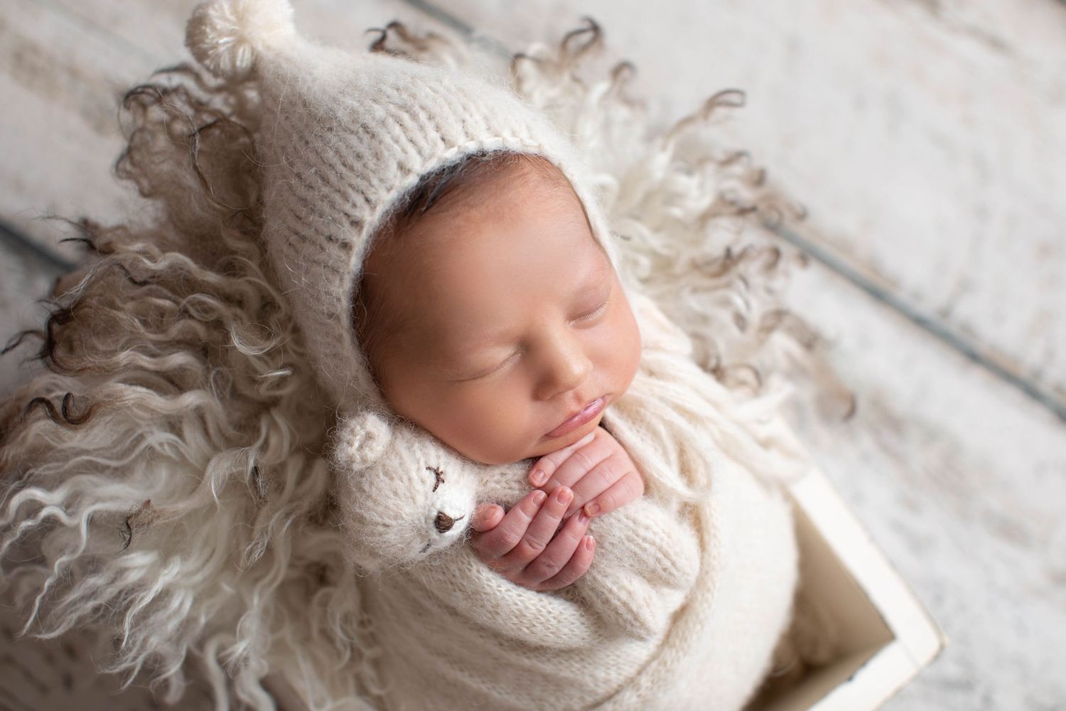 Newborn in knit hat sleeping on fluffy white wool in wooden box. Dubai Photographer