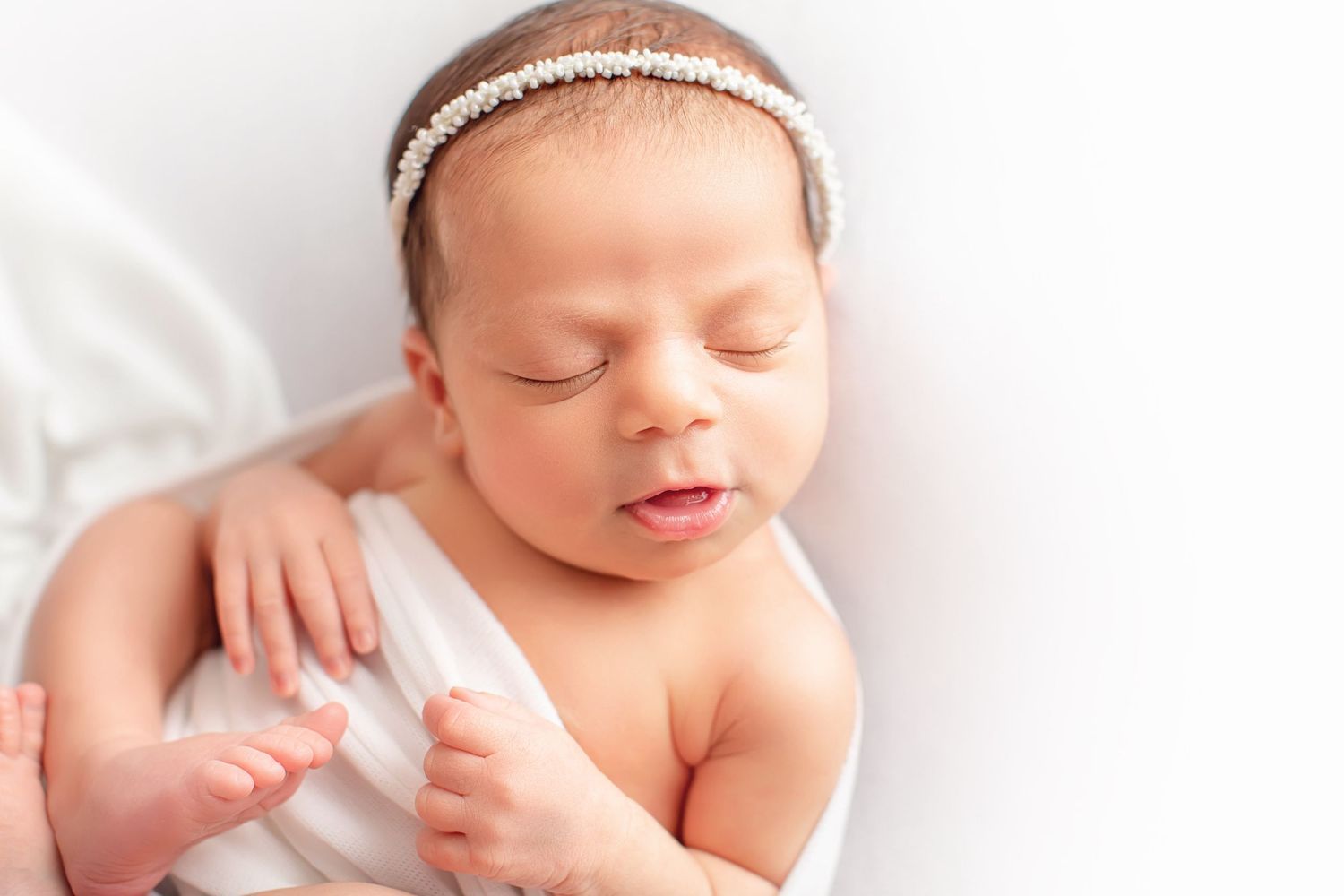 Newborn wearing delicate white headband resting on white blanket. Dubai Photographer