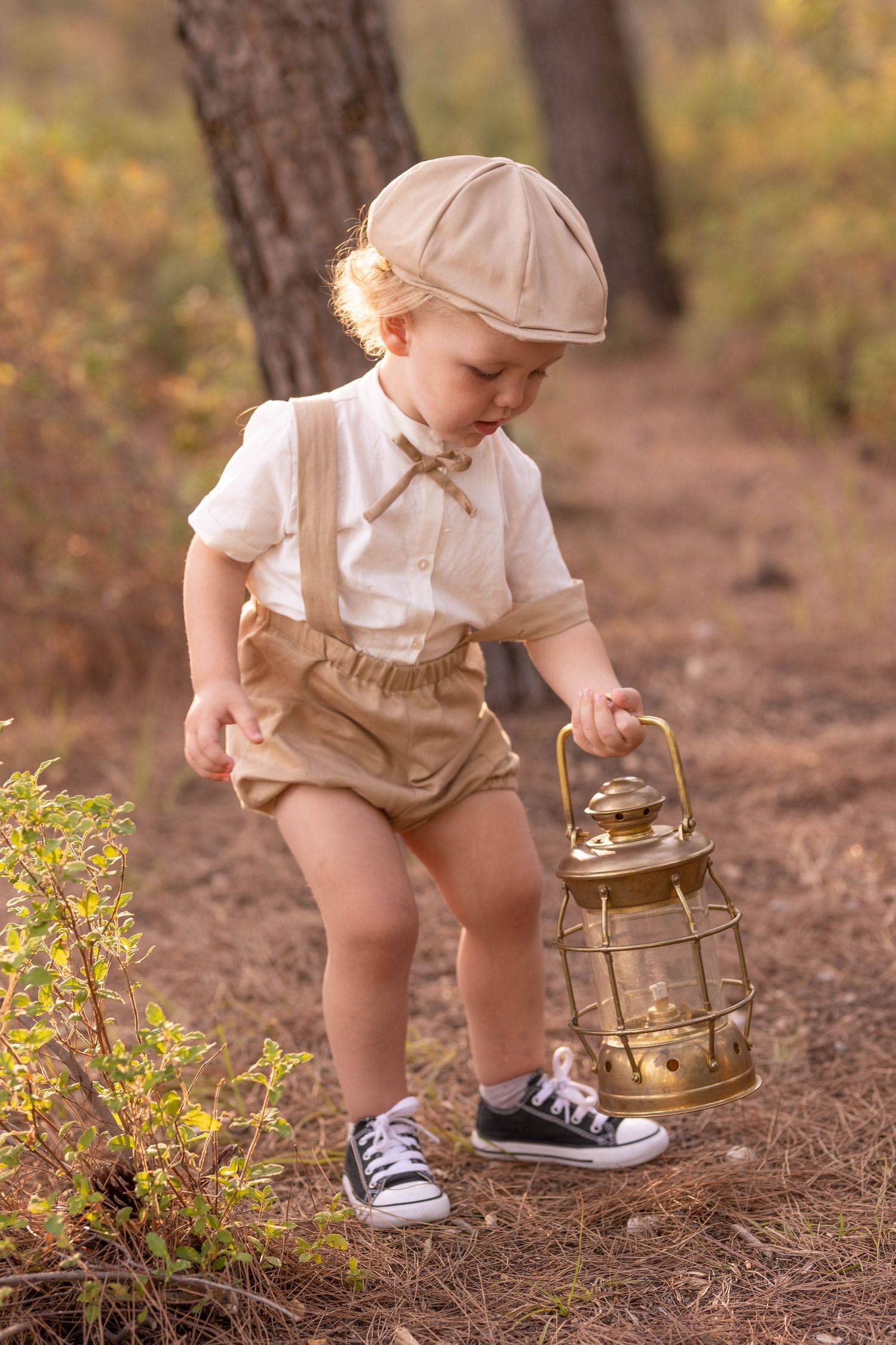 Child in vintage outfit carrying antique lantern along forest trail. Dubai Photographer