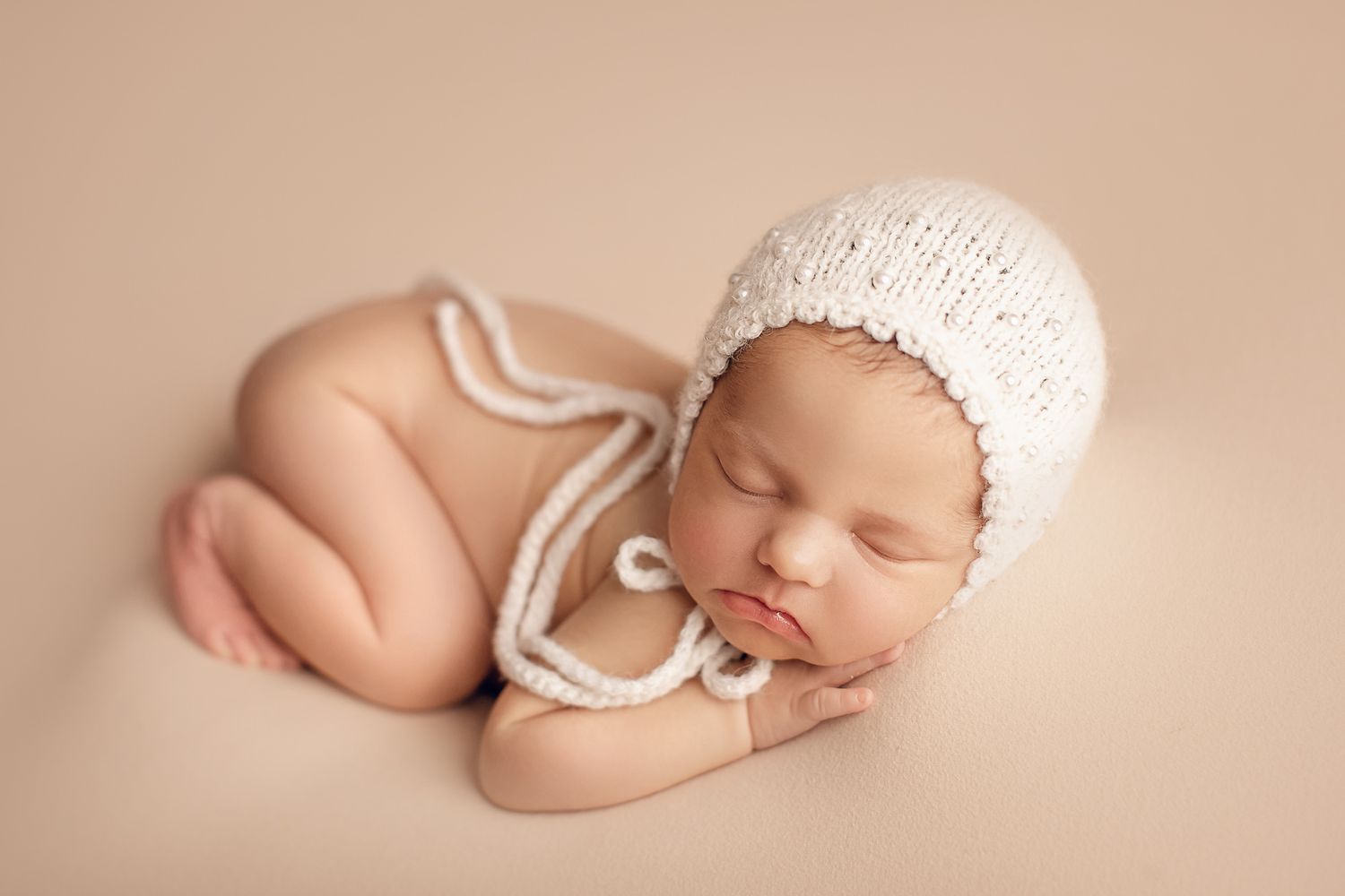 Artistic newborn portrait with baby in cream knit bonnet on beige background. Dubai Photographer