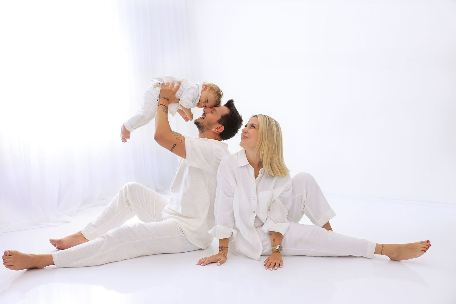 Family wearing white clothes plays together on floor during studio photoshoot. Dubai Photographer