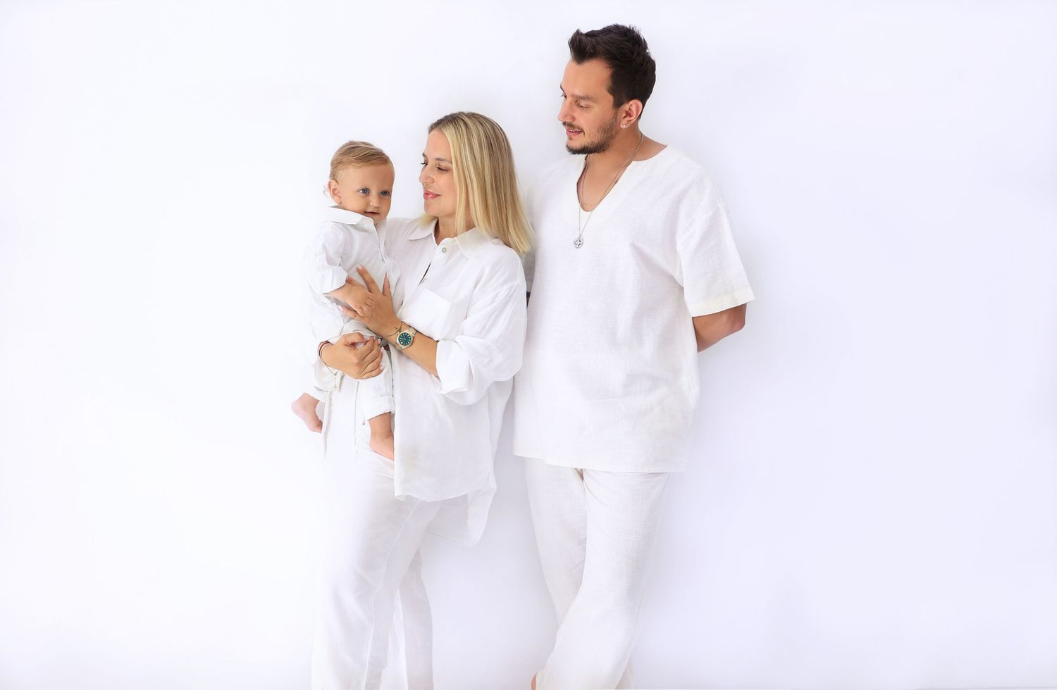 Family of three dressed in matching white outfits poses against white background. Dubai Photographer