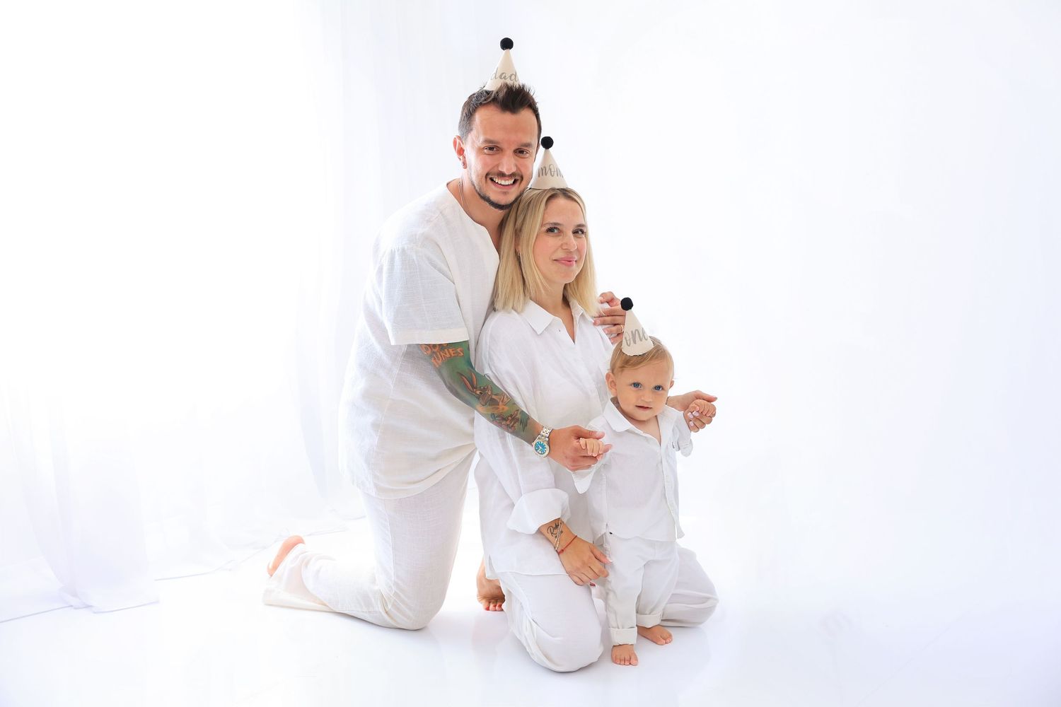 Family dressed in white shares tender moment against bright white studio background. Dubai Photographer
