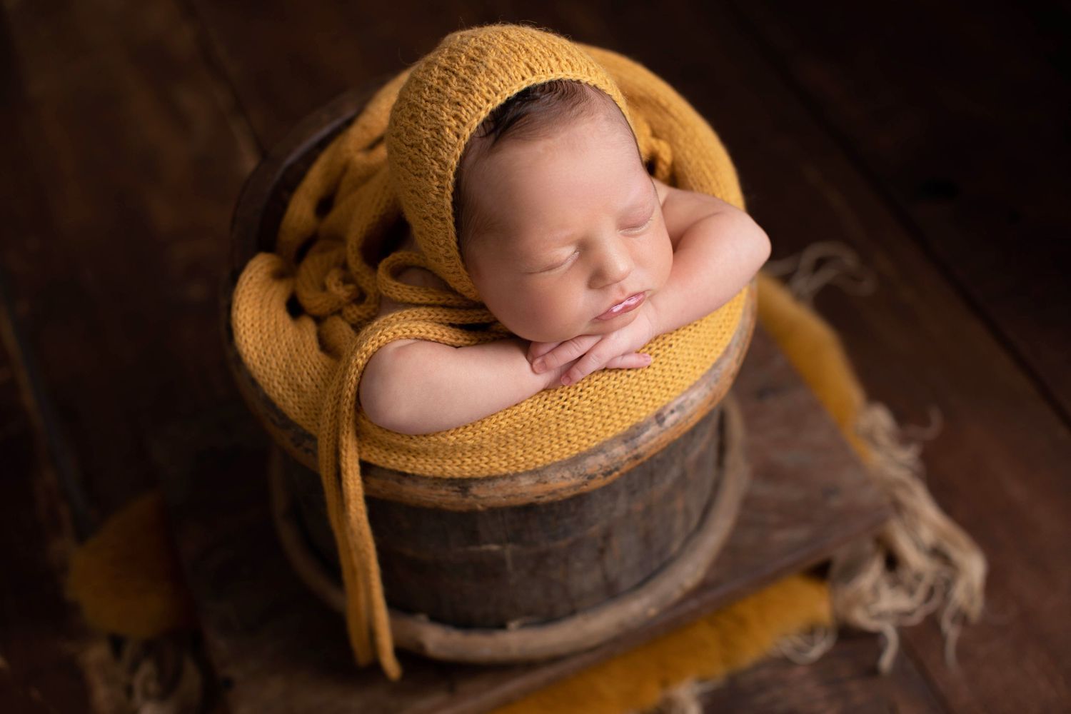 Newborn sleeping in wooden barrel with mustard yellow wrap and blanket. Dubai Photographer