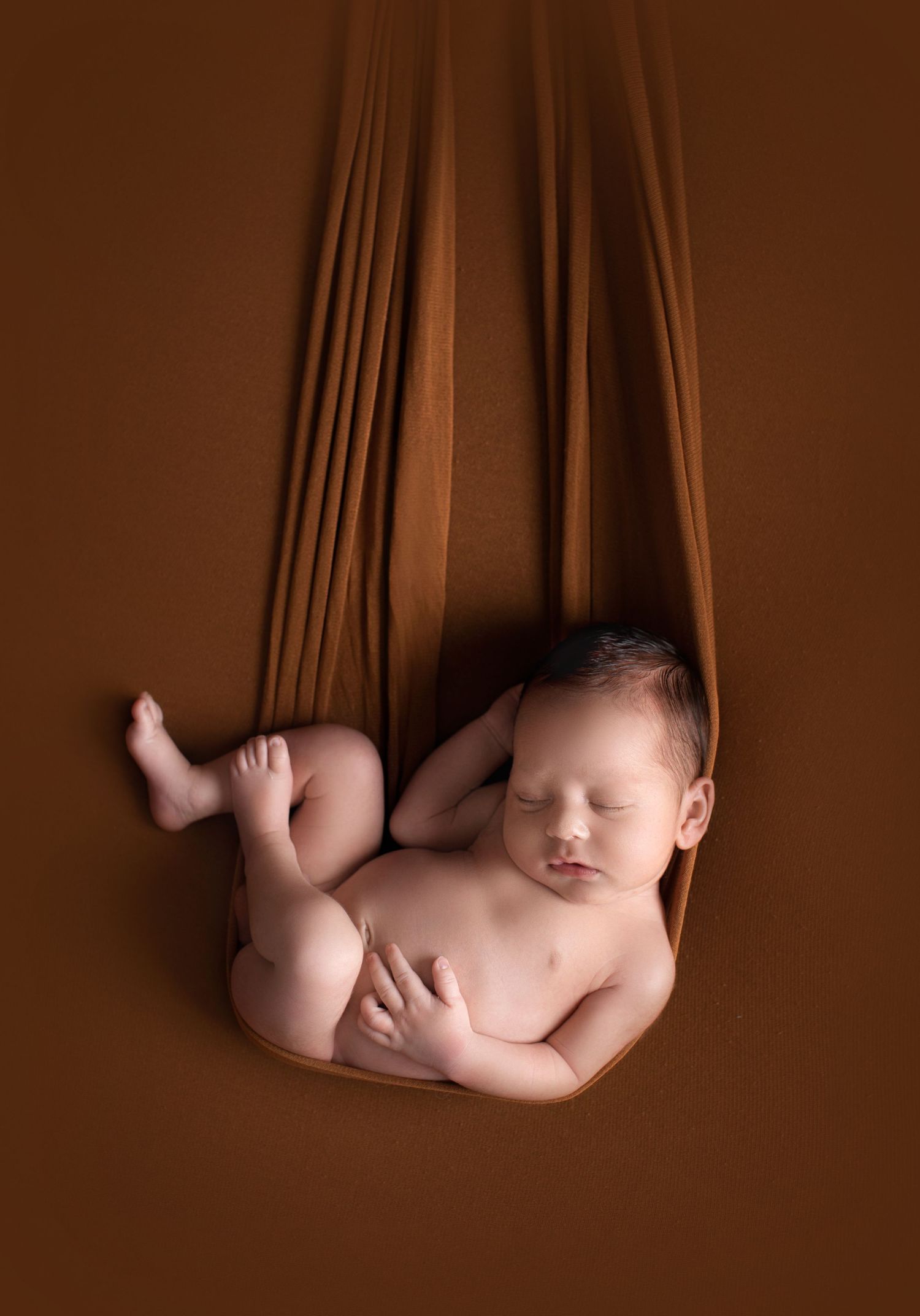 Peaceful sleeping newborn nestled in brown fabric hammock. Dubai Photographer