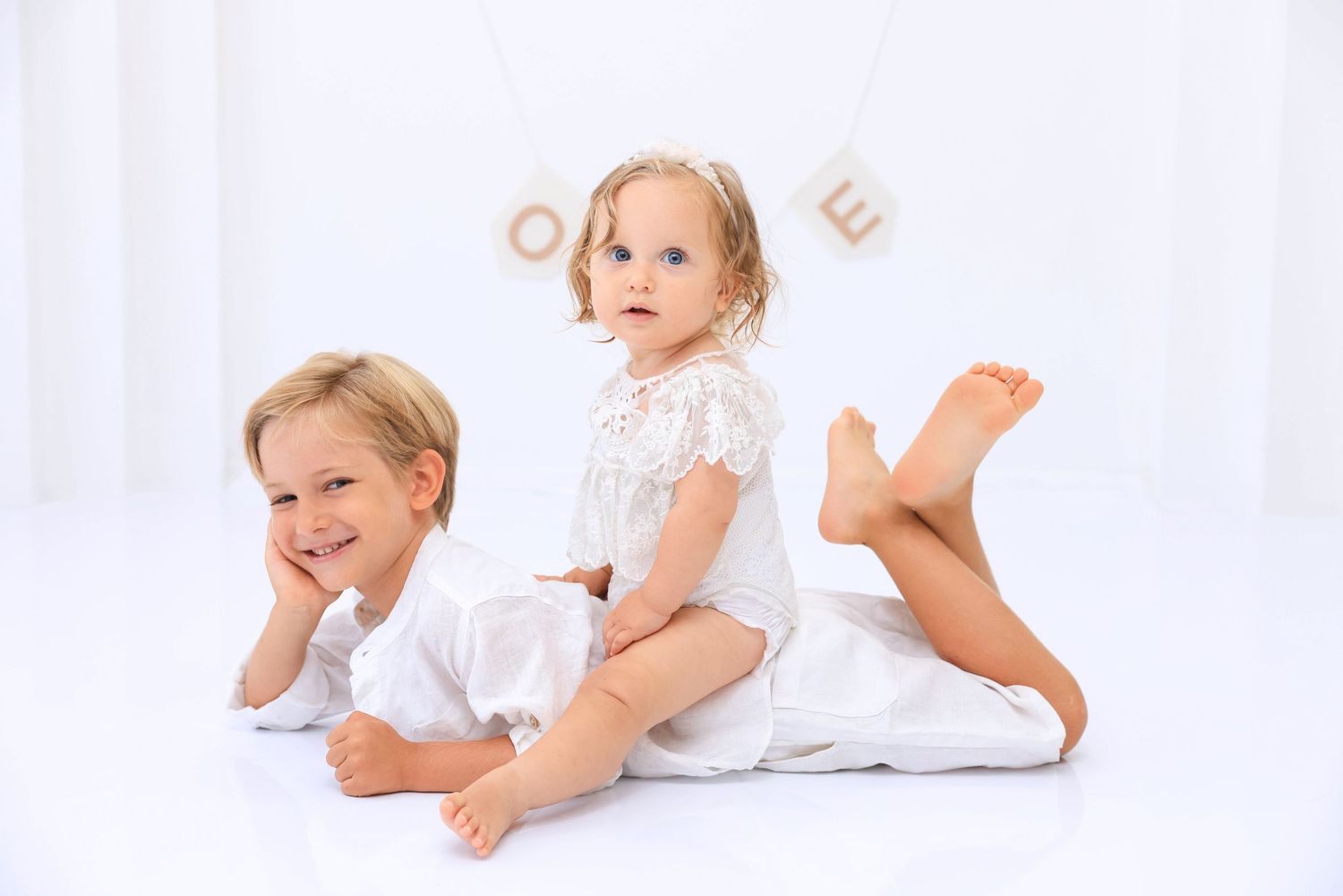 Three sequential photos showing a baby in white clothing lying on their tummy and playing on a white background. Dubai Photographer