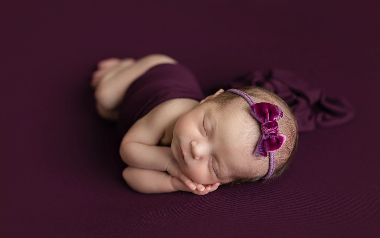Sleeping newborn with purple bow on dark purple background. Dubai Photographer