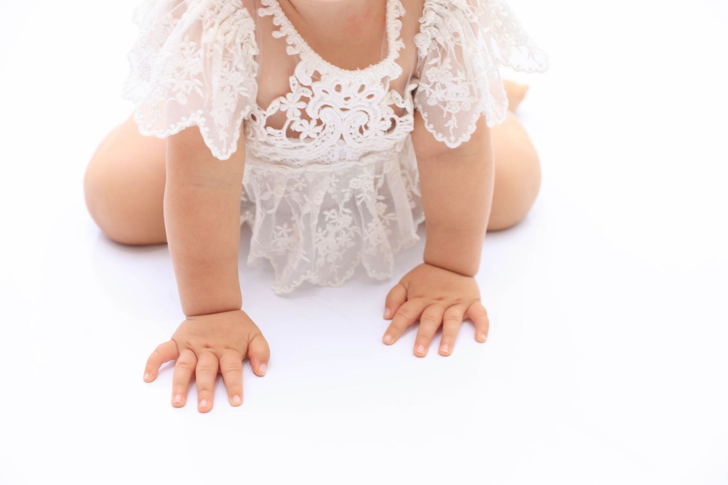 Three identical baby dolls wearing white lace dresses sit in a row on a light surface. Dubai Photographer