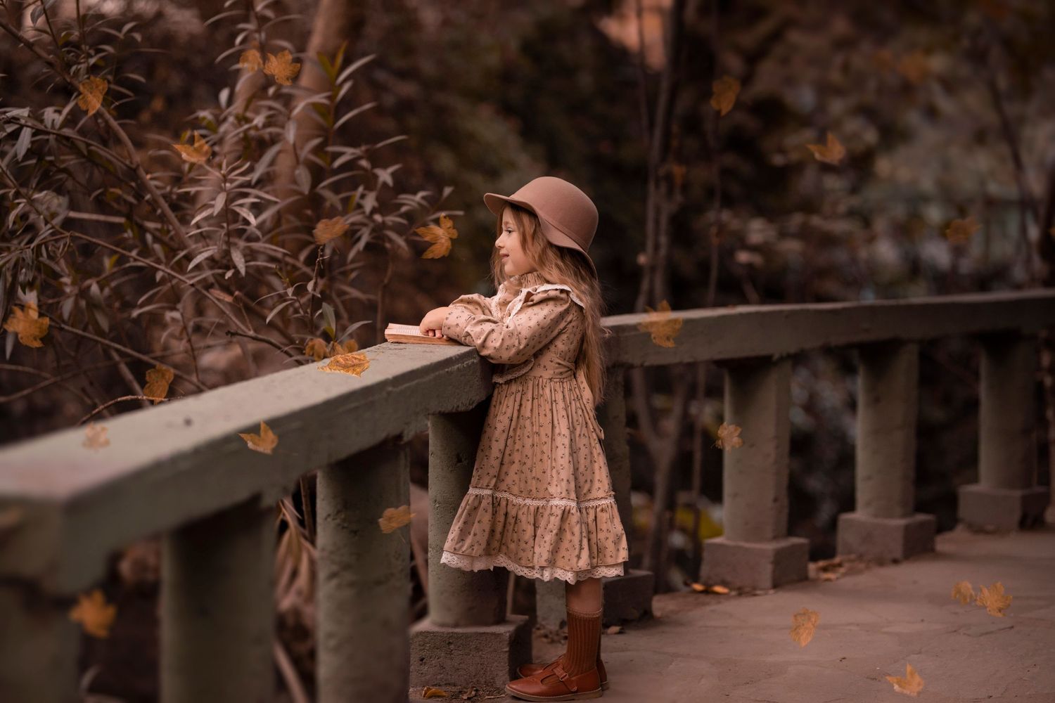 Atmospheric autumn scene with a figure in a brown dress and hat leaning against a stone bridge railing. Dubai Photographer