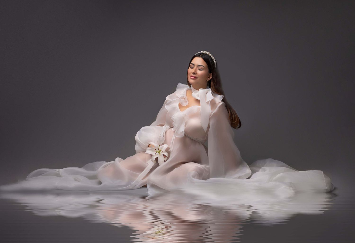 Maternity portrait with flowing white fabric creating reflection effect on dark background. Dubai Photographer
