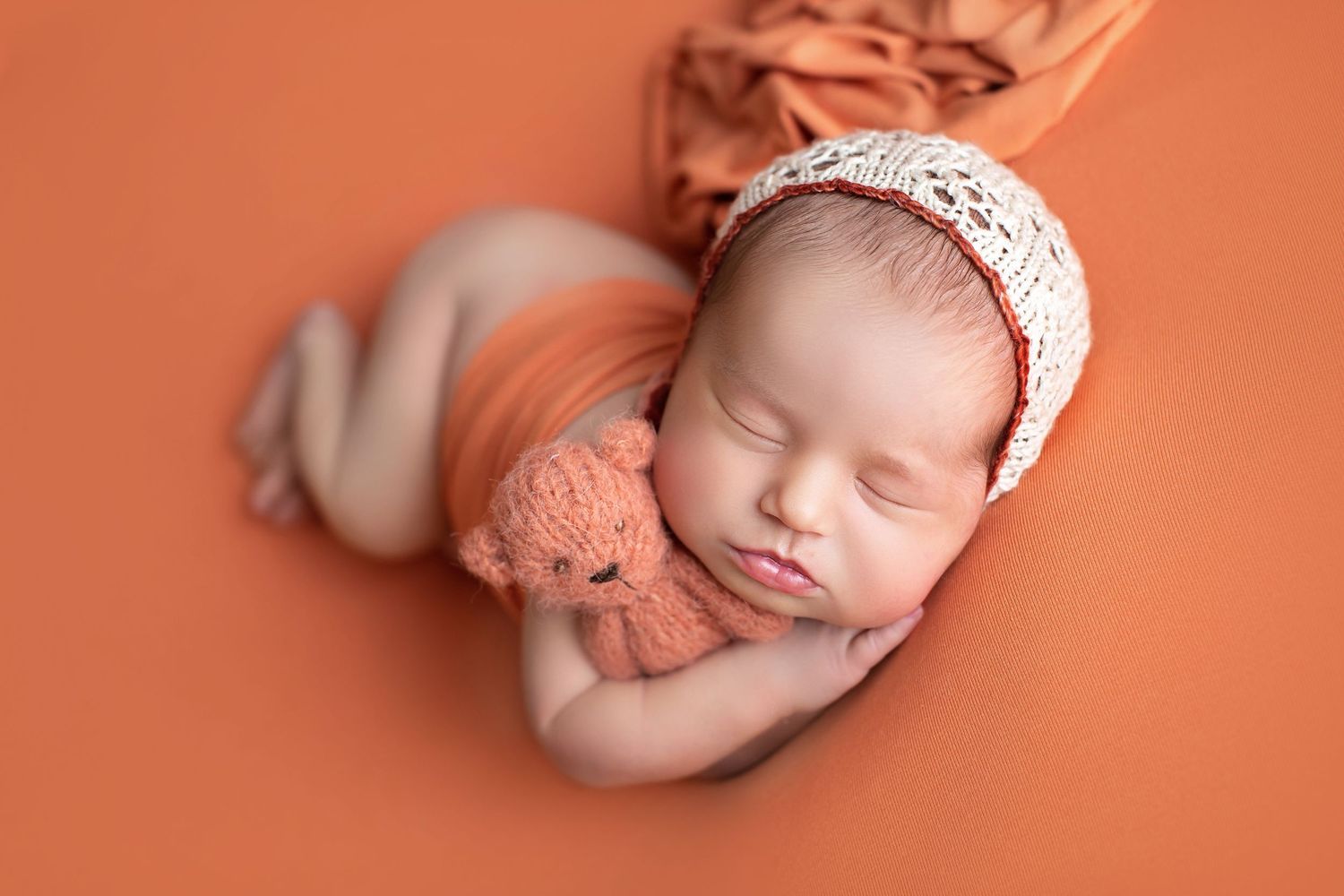 Peaceful newborn baby sleeping on coral background with knit bonnet and teddy bear. Dubai Photographer