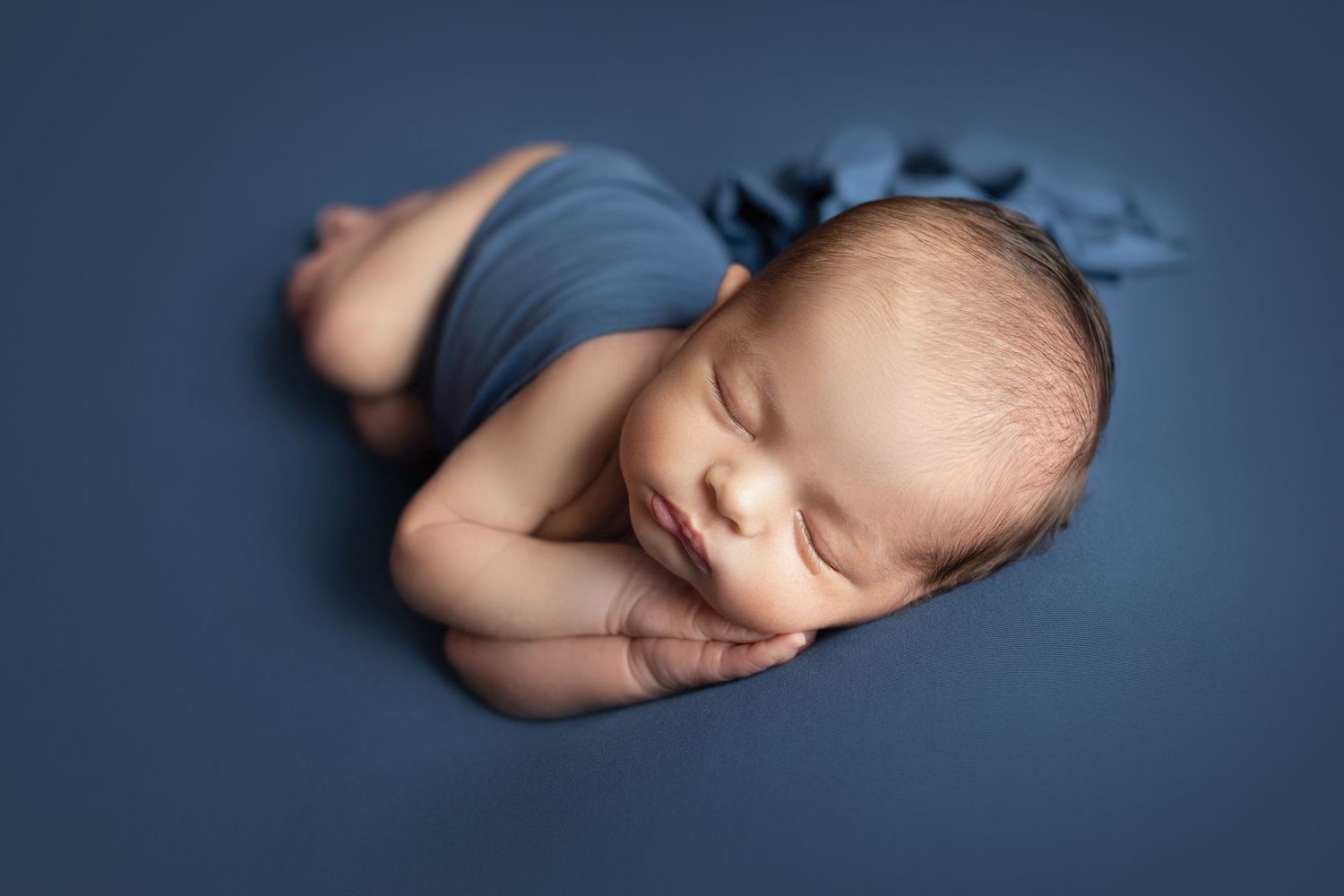 Peaceful sleeping newborn wrapped in navy blue fabric against dark blue background. Dubai Photographer