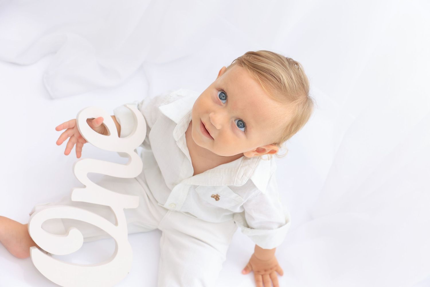 Child in white clothing plays with decorative letters against white backdrop. Dubai Photographer