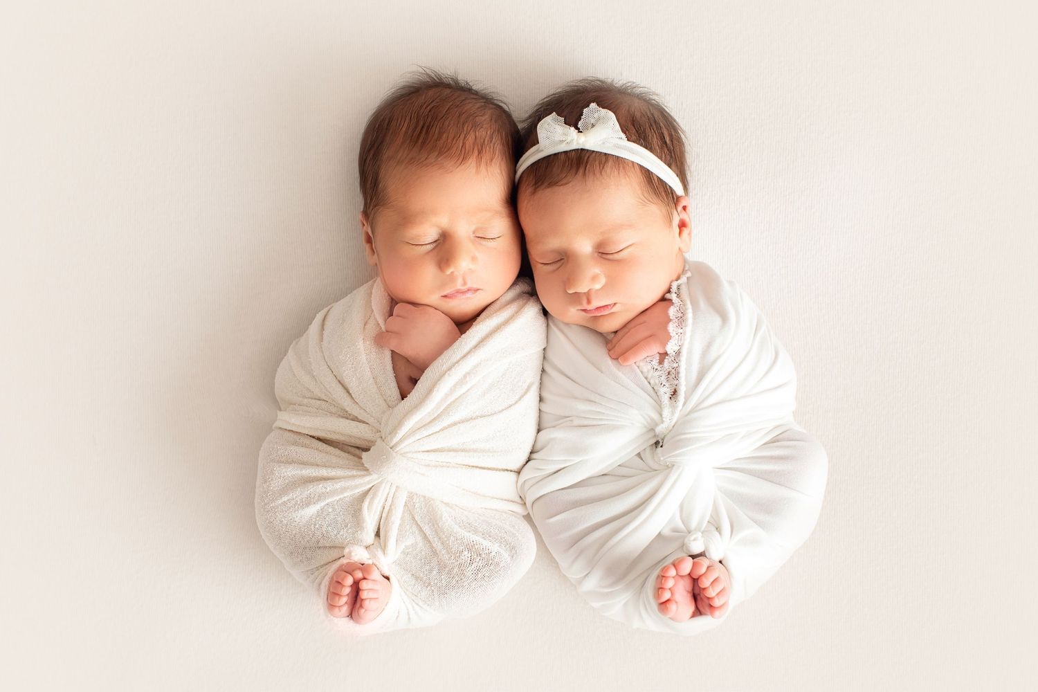 Twin newborns wrapped in white swaddles sleeping side by side. Dubai Photographer