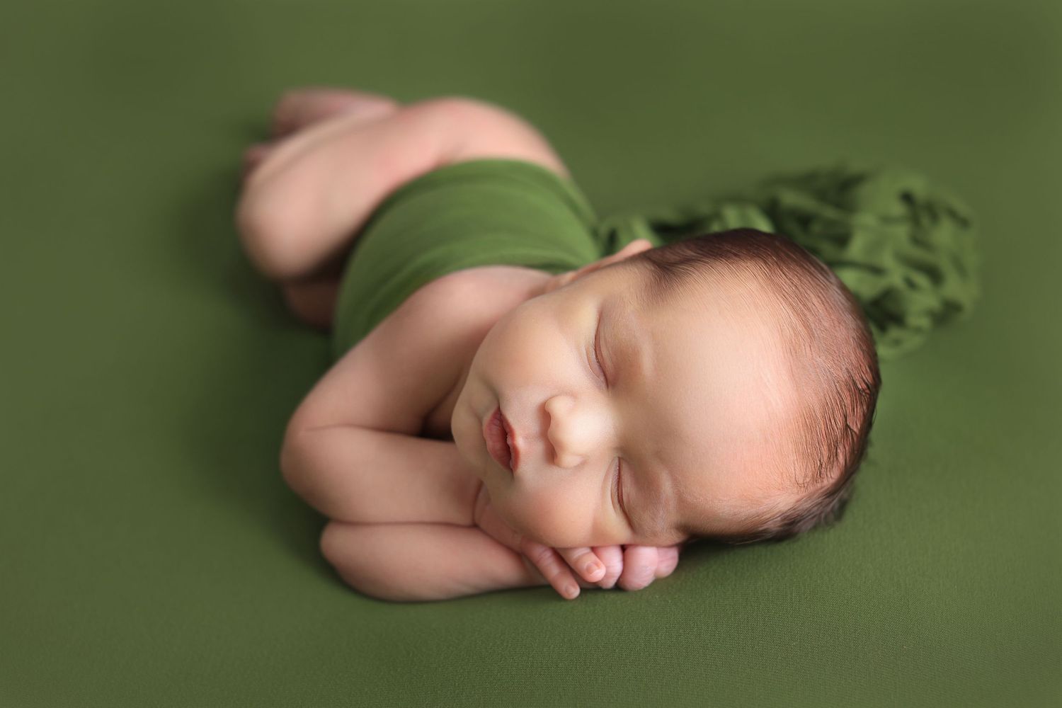 Sleeping newborn wearing green wrap on olive green textured background. Dubai Photographer