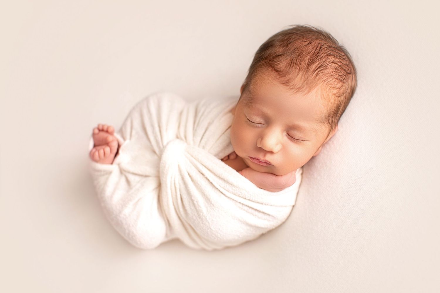 Newborn wrapped in white fabric sleeping peacefully on light backdrop. Dubai Photographer