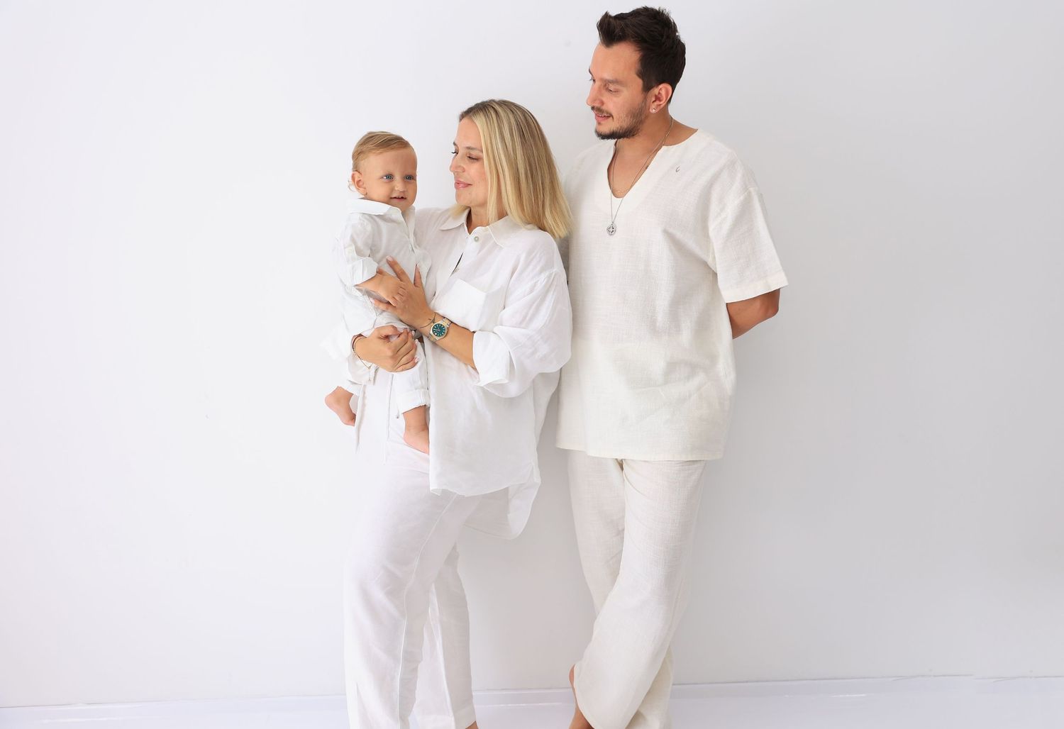 Family wearing coordinated white outfits poses together against white background. Dubai Photographer