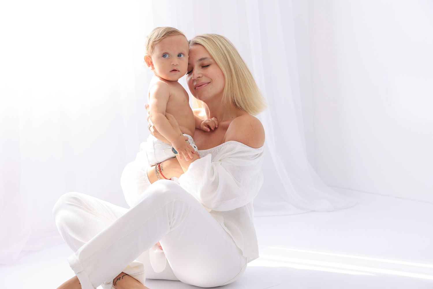 Mother and baby share intimate moment on white backdrop in matching white outfits. Dubai Photographer