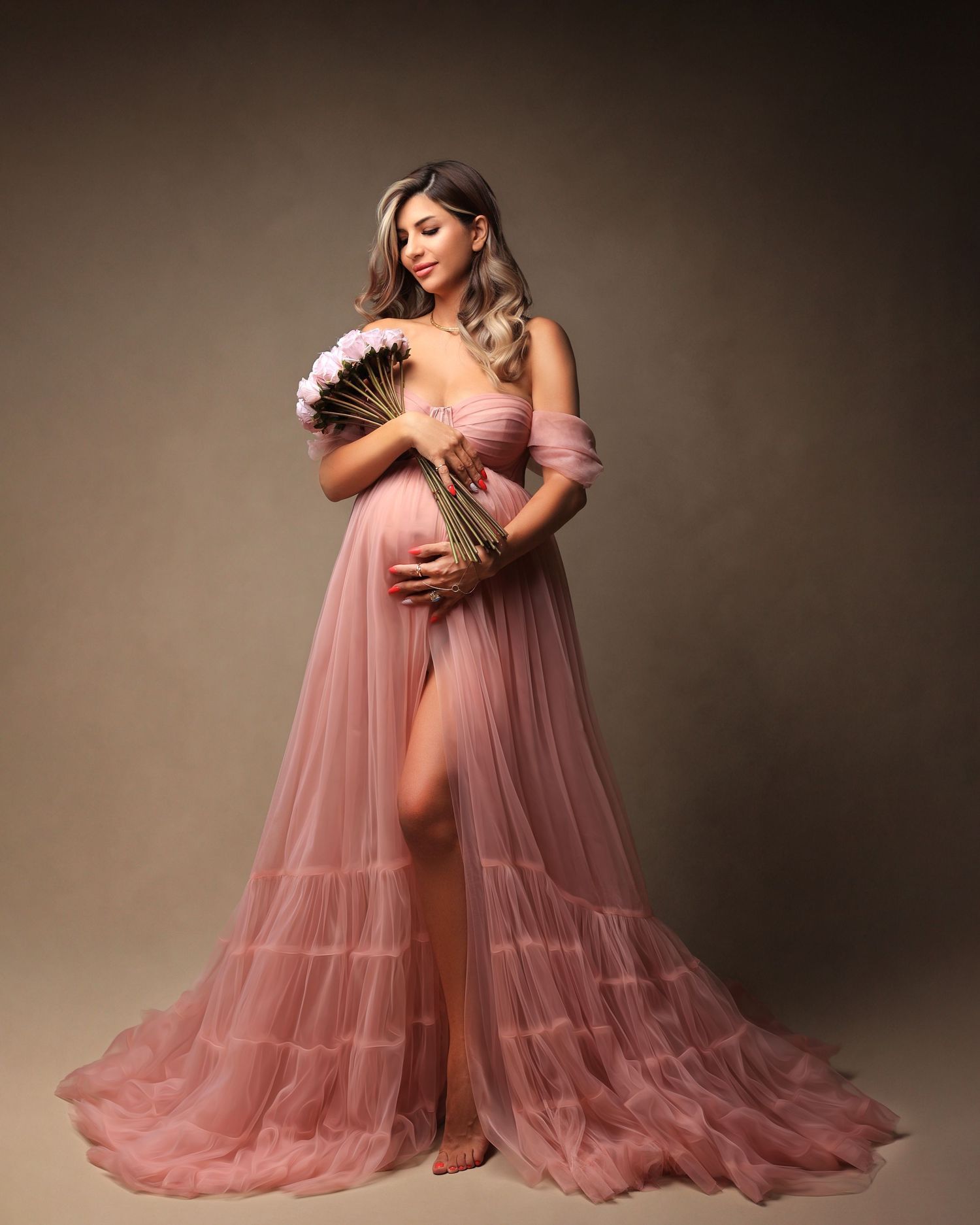 Maternity photo of woman in flowing pink tulle gown holding dried palm fronds. Dubai Photographer