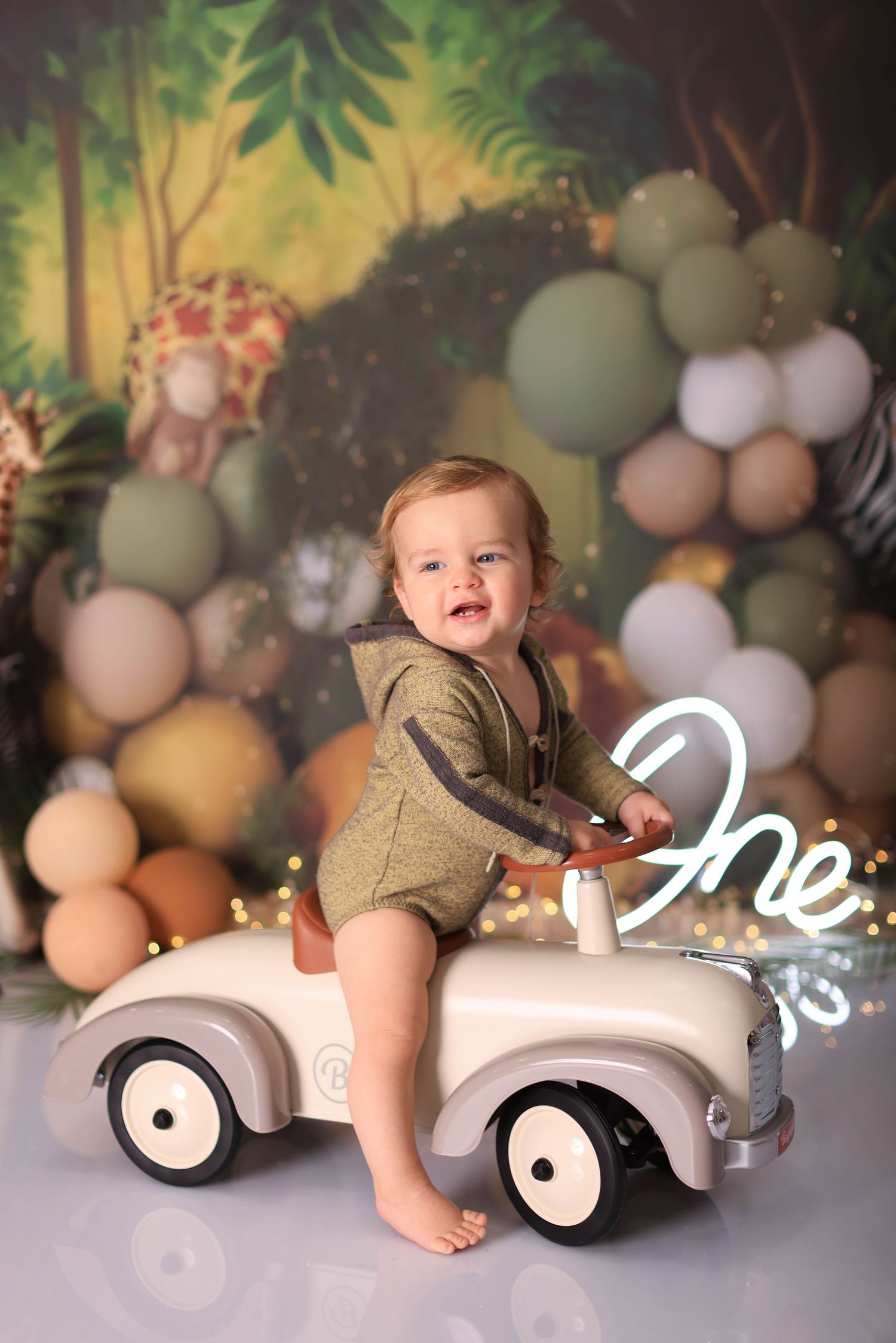 Four sequential photos of a baby sitting and playing on a vintage toy car against a dreamy backdrop with balloons and foliage. Dubai Photogr