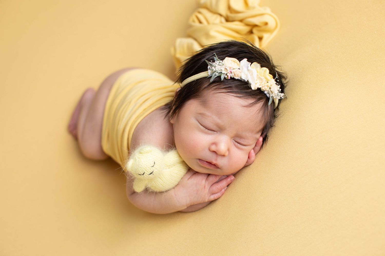 Sleeping newborn in yellow wrap with floral headband resting on yellow backdrop. Dubai Photographer