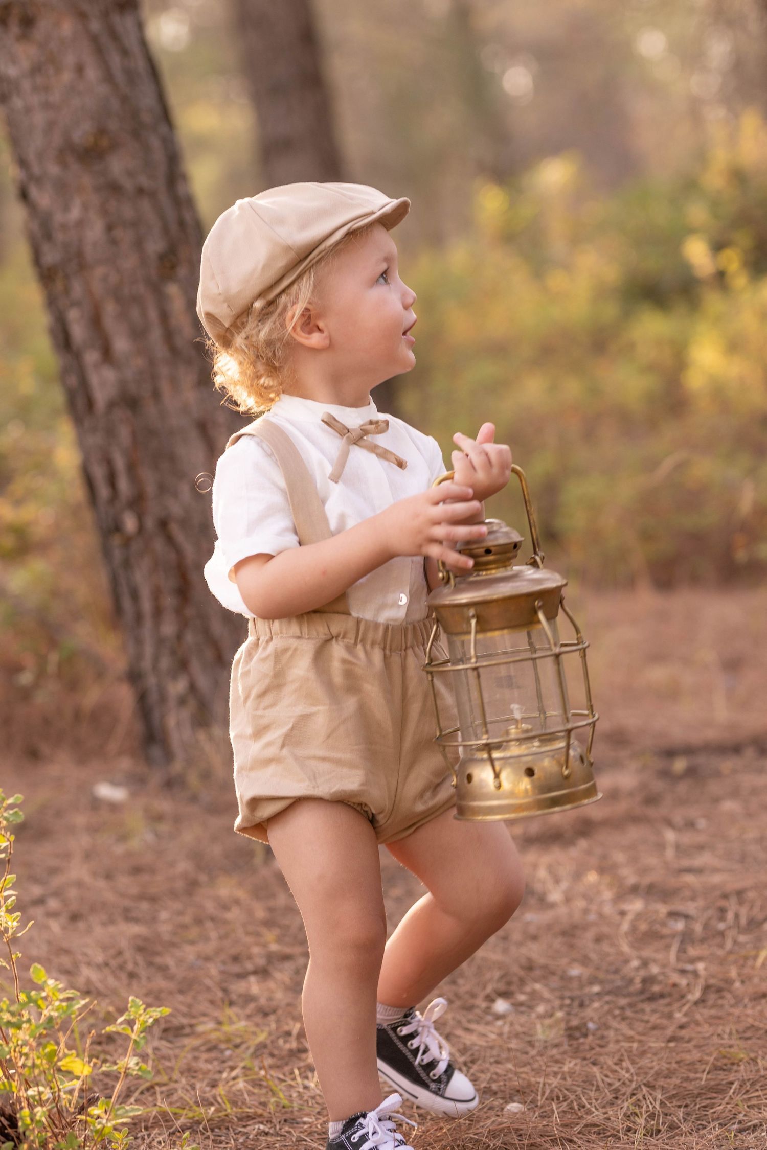 Child exploring forest path while holding vintage lantern in retro-styled clothing. Dubai Photographer