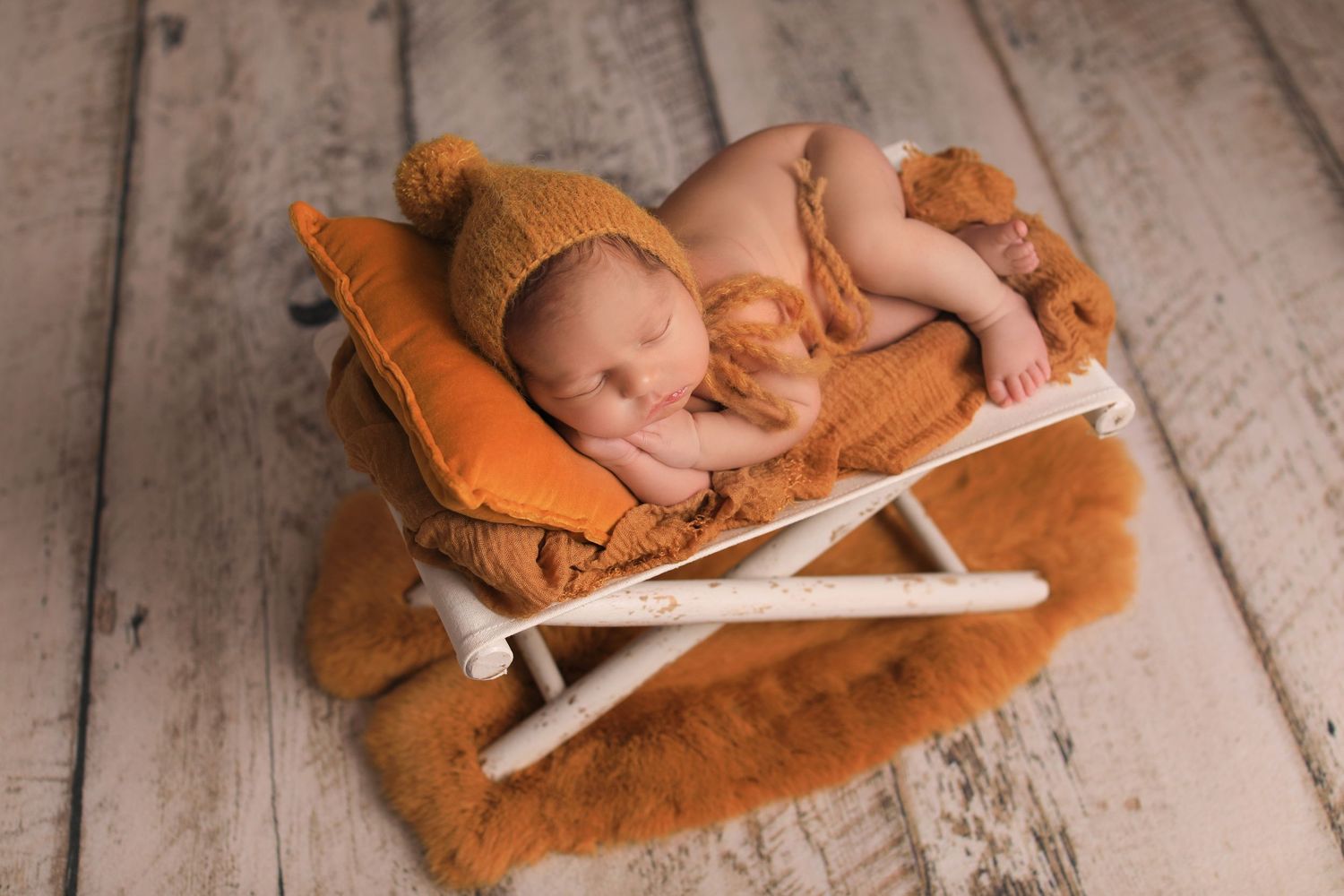 Peaceful newborn sleeping on orange cushioned lounger against rustic wooden backdrop. Dubai Photographer