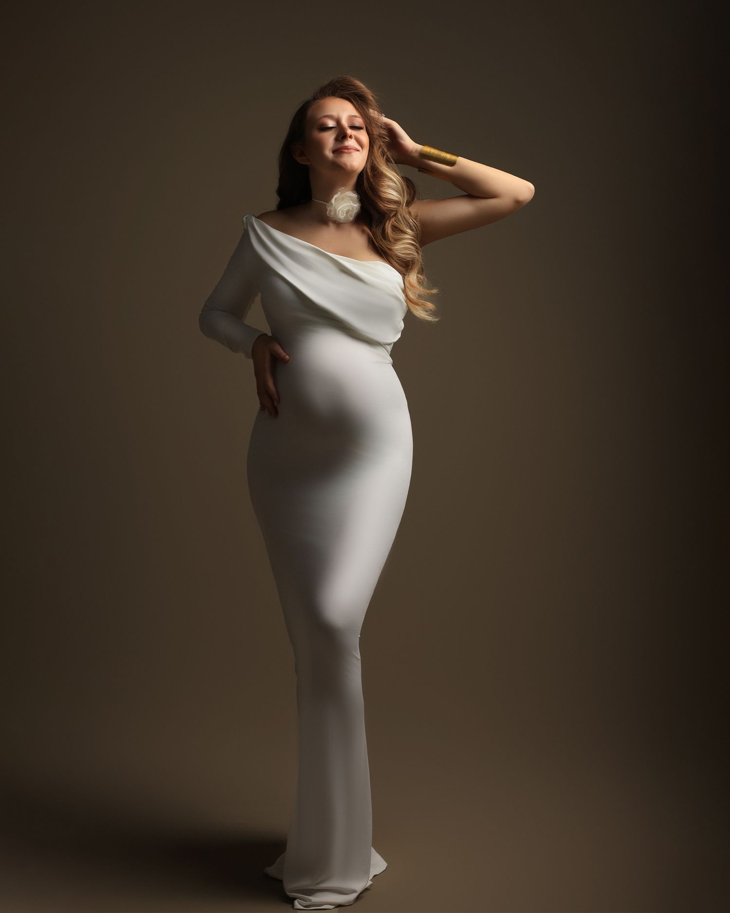 Sophisticated maternity portrait in fitted white gown with asymmetrical neckline. Dubai Photographer
