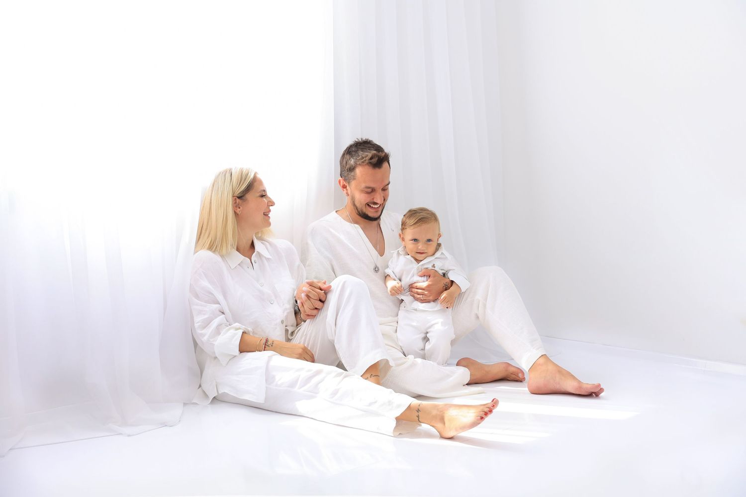 Family relaxes together on floor during minimalist white-themed photo session. Dubai Photographer