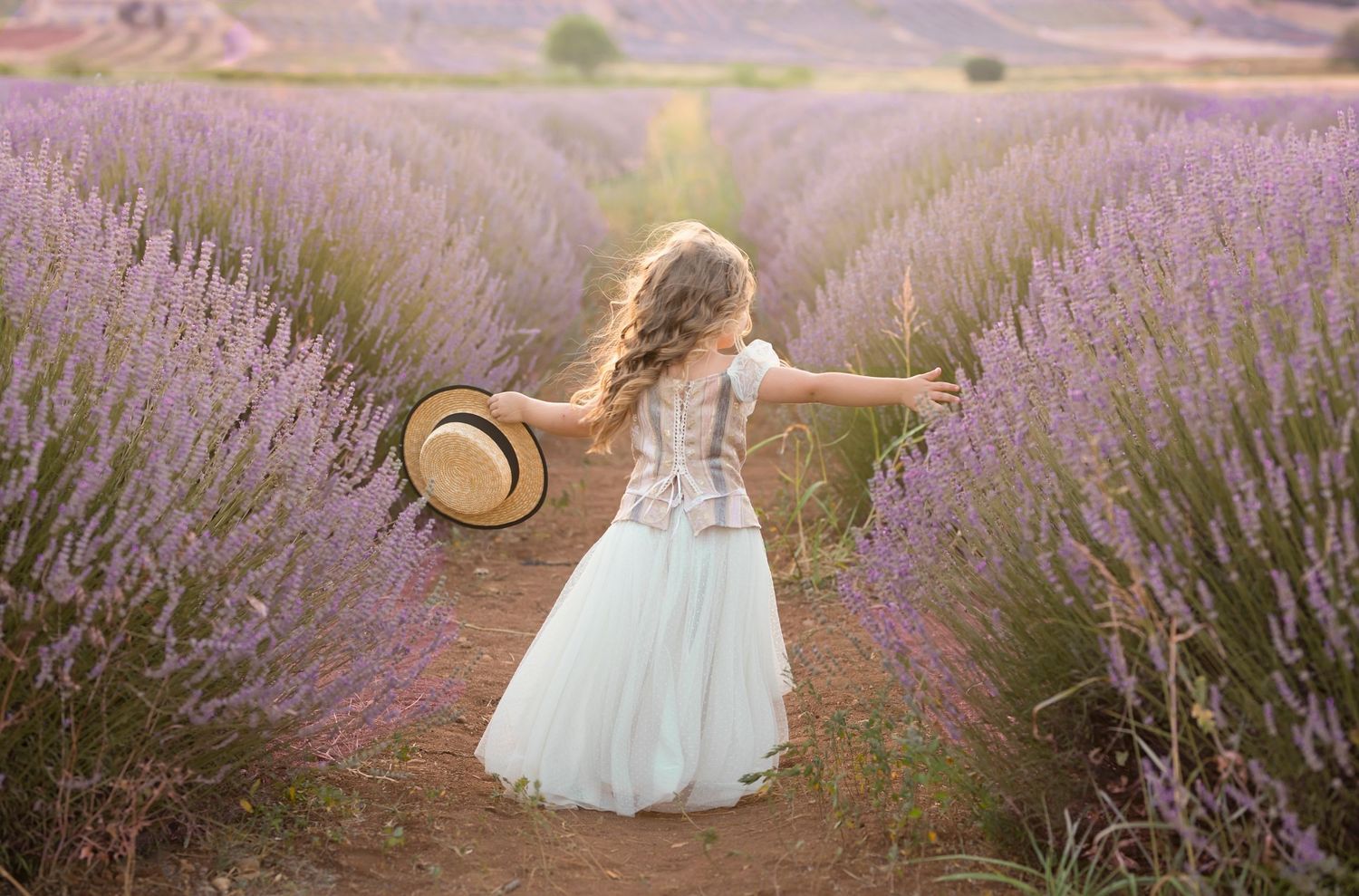 White dress-clad figure with arms spread wide in a blooming lavender field at sunset. Dubai Photographer