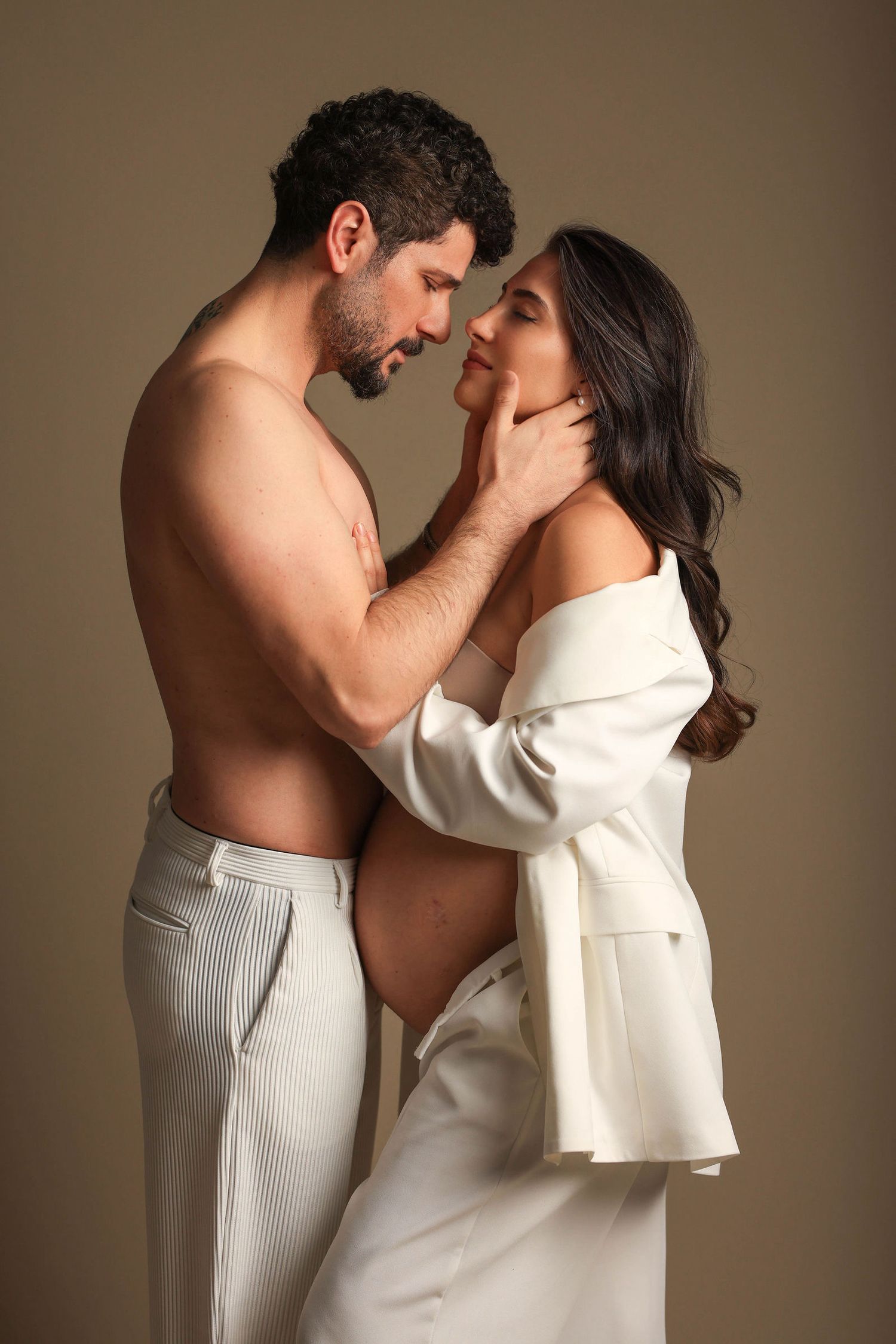 Intimate couple poses in romantic studio portrait with warm brown background and soft lighting.Dubai Photographer