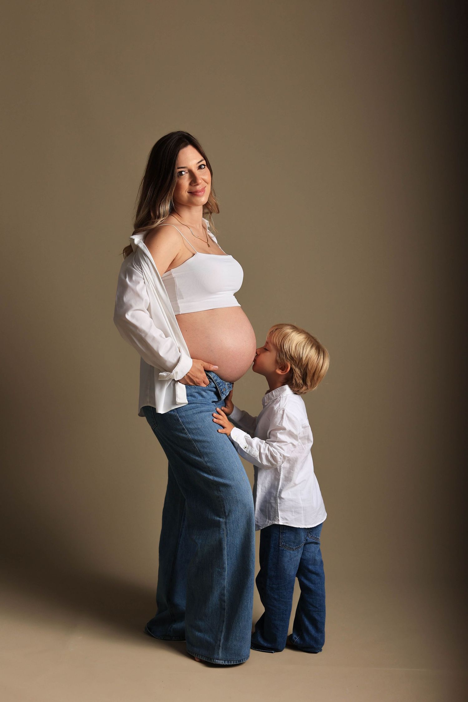 A tender maternity photo series shows a child in white kissing a pregnant belly while wearing matching blue denim.Dubai Photographer