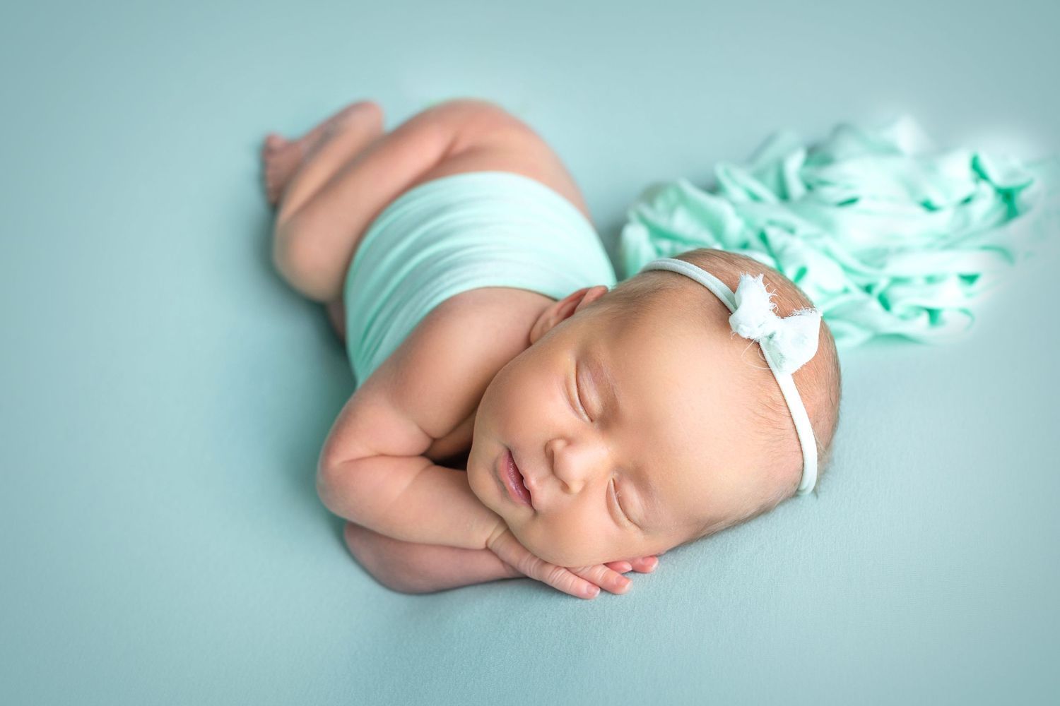 Sleeping newborn wearing mint wrap on light blue background with flowing fabric. Dubai Photographer