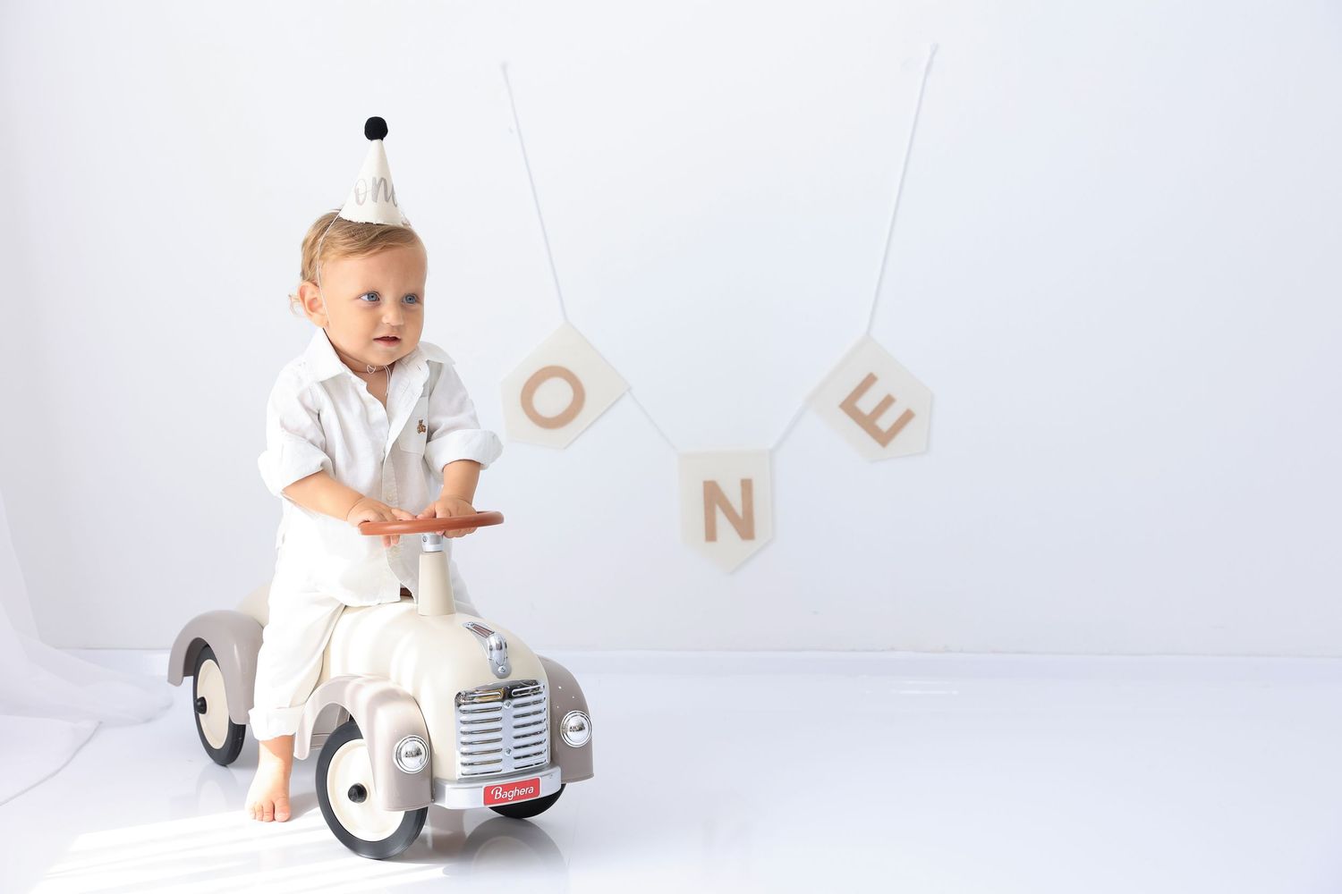 Young child rides vintage-style toy car beneath hanging letters on white background. Dubai Photographer