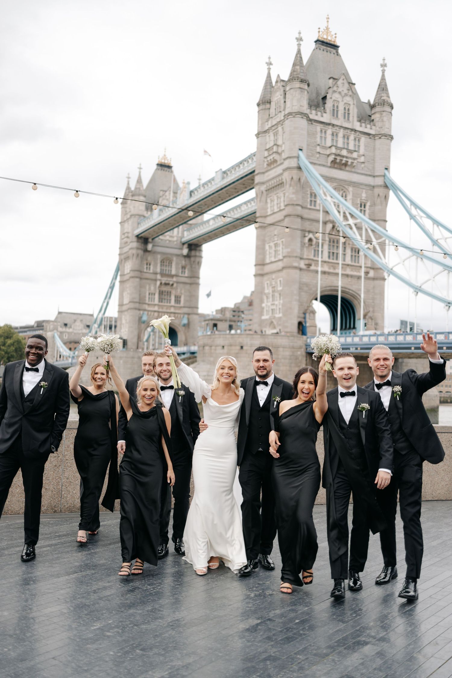 Wedding party posing together in formal attire in front of London's iconic Tower Bridge.