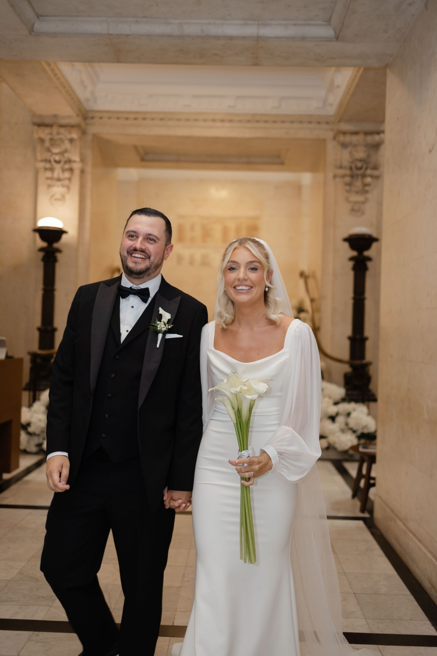 Elegant wedding couple walking through marble hallway with classic architecture.