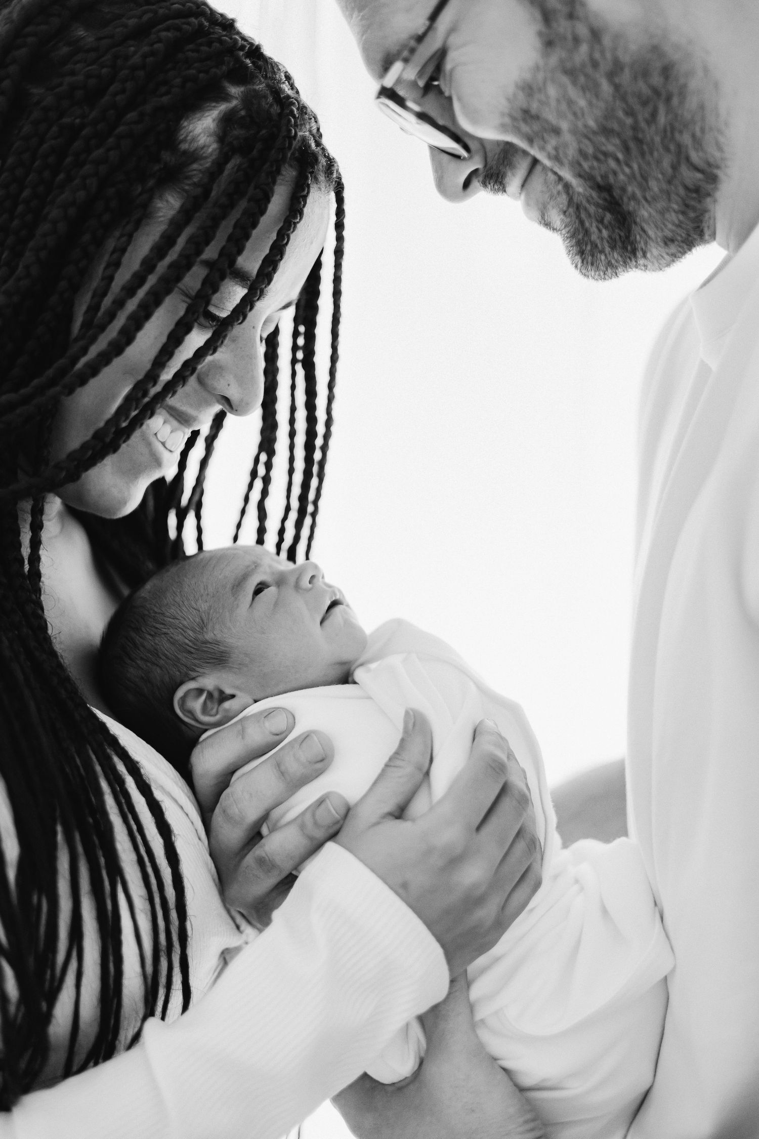 Intimate black and white newborn photography session with gentle parental embrace.
