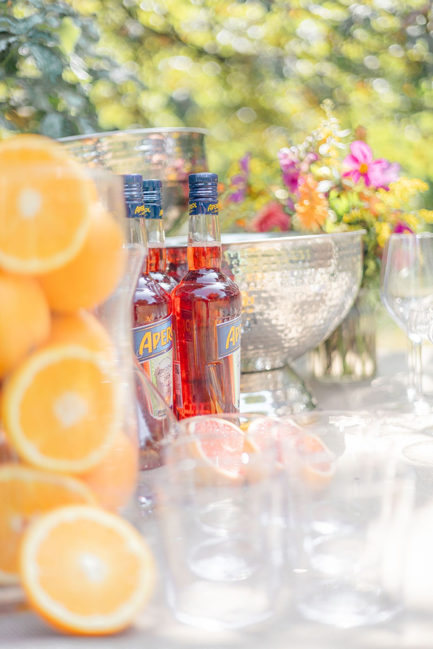 Refreshment table with soft drinks, citrus fruits and crystal glassware at an outdoor party.
