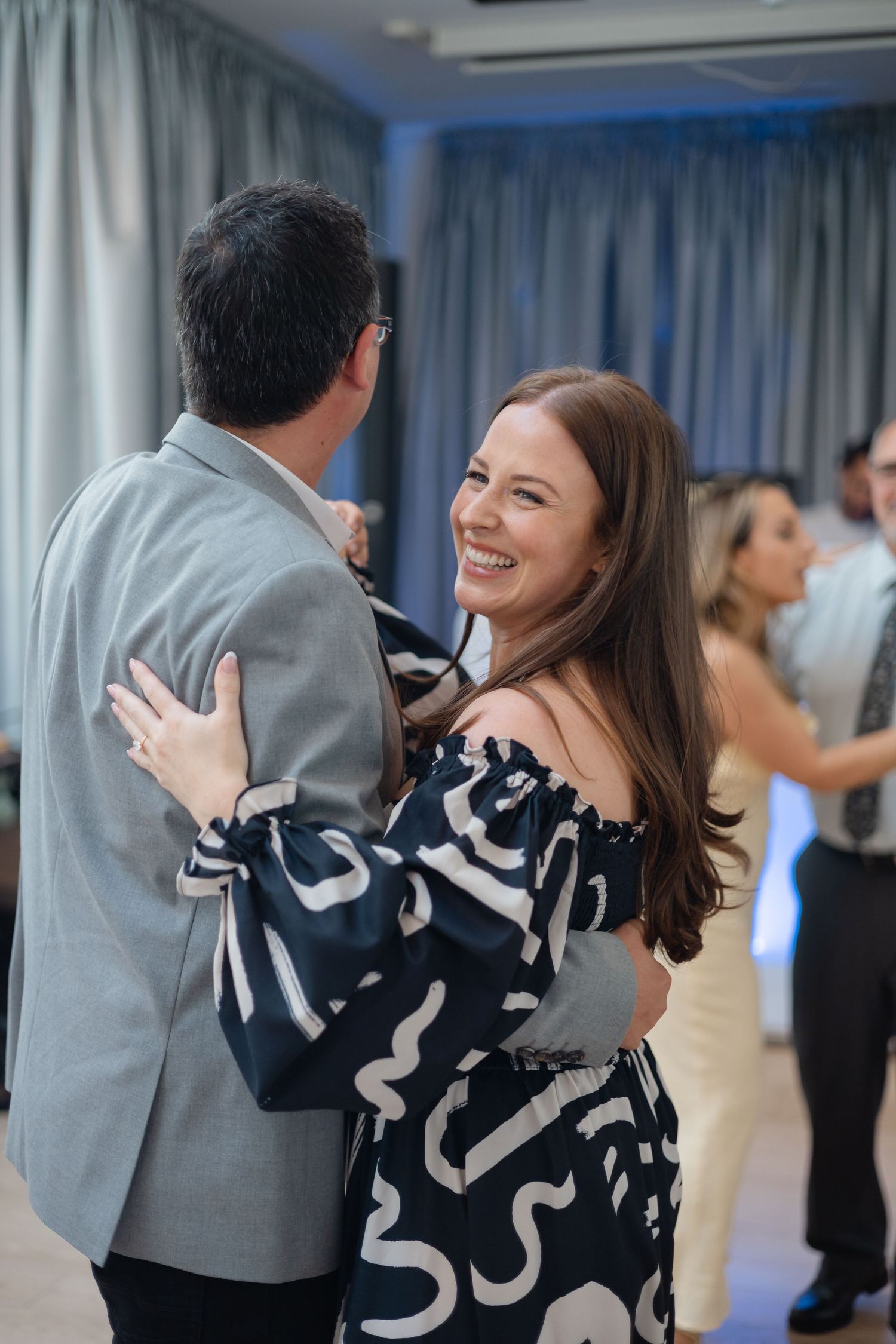 Couples dance together during a social gathering with blue curtains in the background.