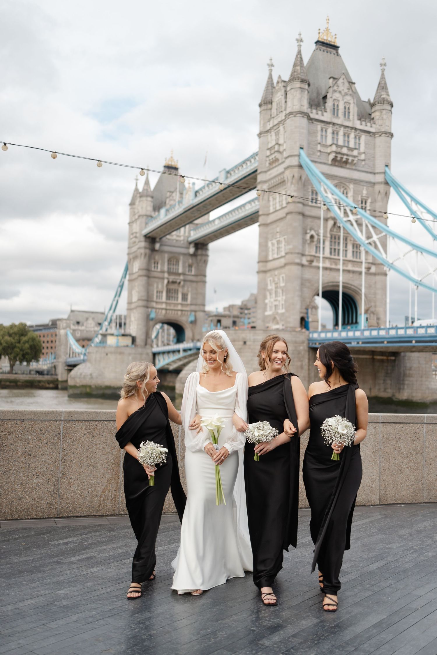 Bridal party in black and white dresses posing in front of London's Tower Bridge.