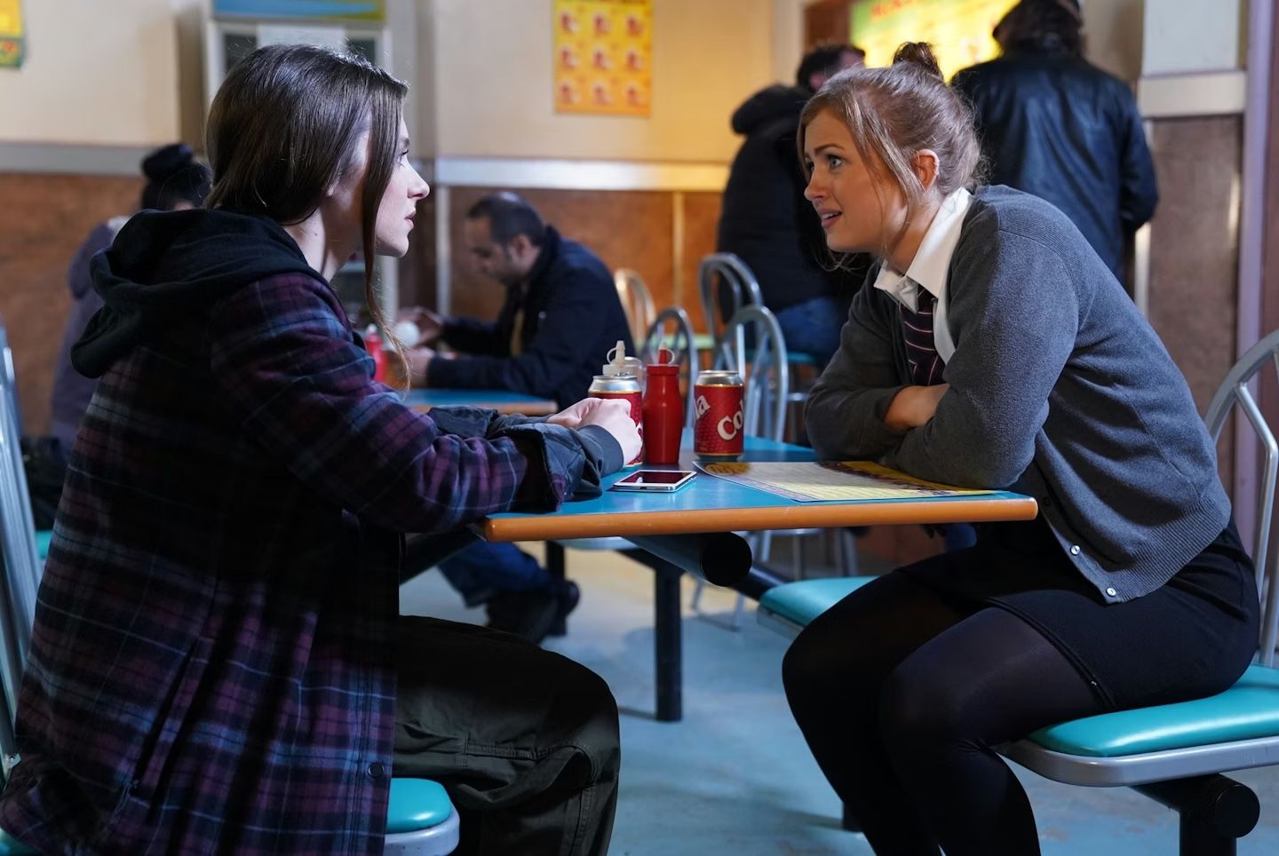 Students sit at tables in a school cafeteria during lunch period while wearing uniforms.