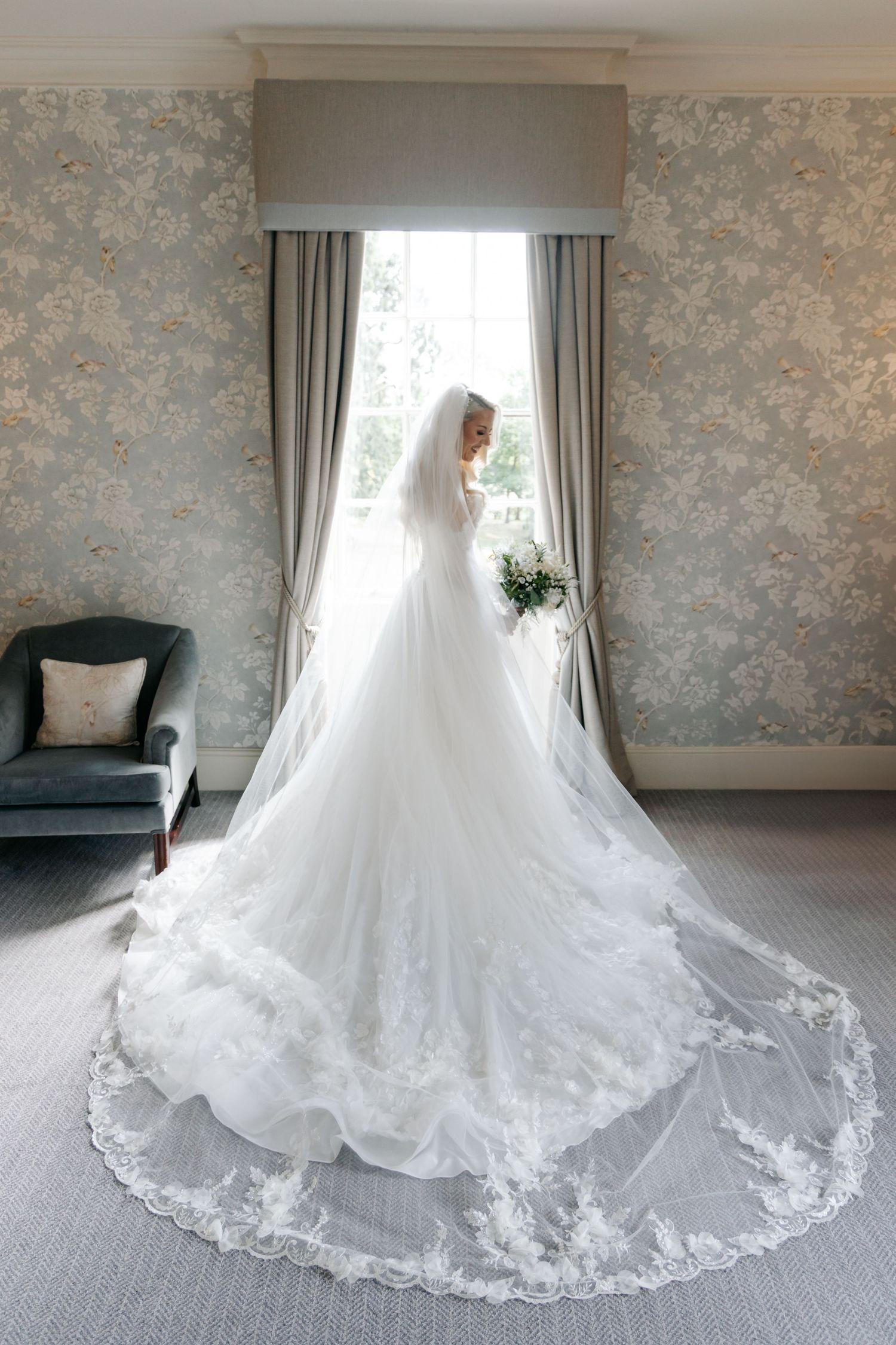 Elegant white wedding dress with intricate lace train displayed in a light-filled room.