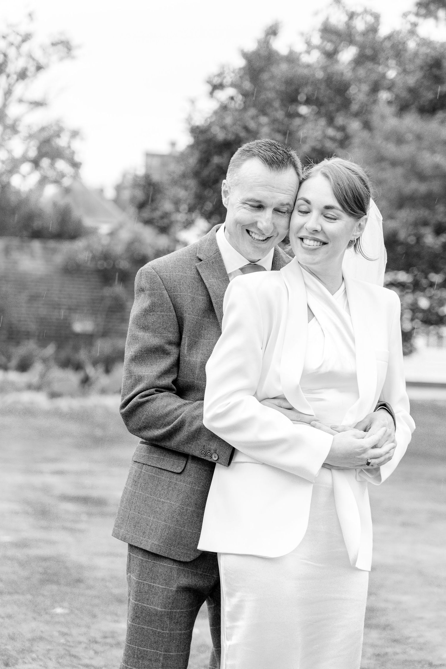 A black and white portrait of a couple in formal attire embracing outdoors.
