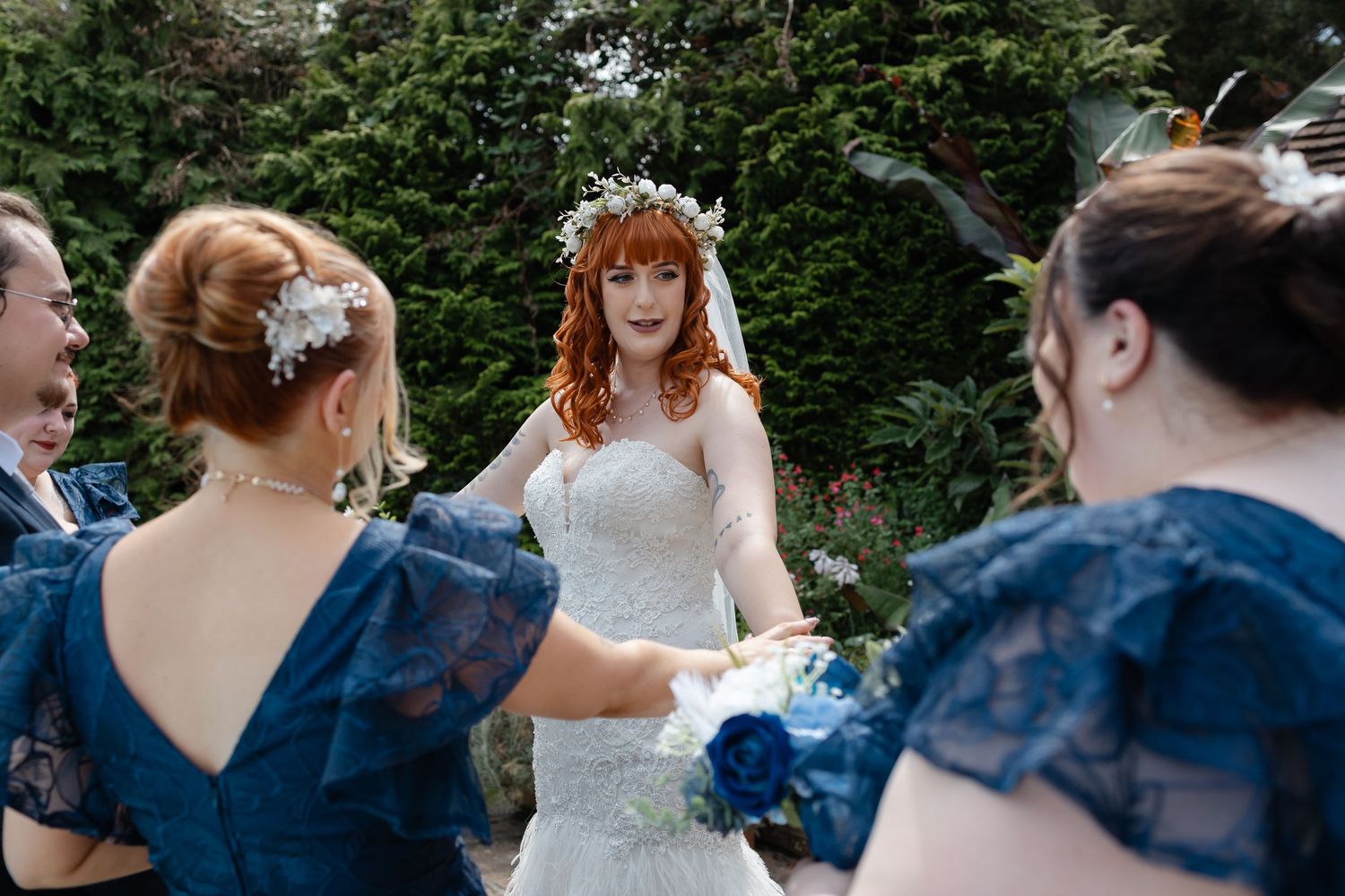 Wedding party in navy blue dresses and white gown photographed from behind in a garden setting.
