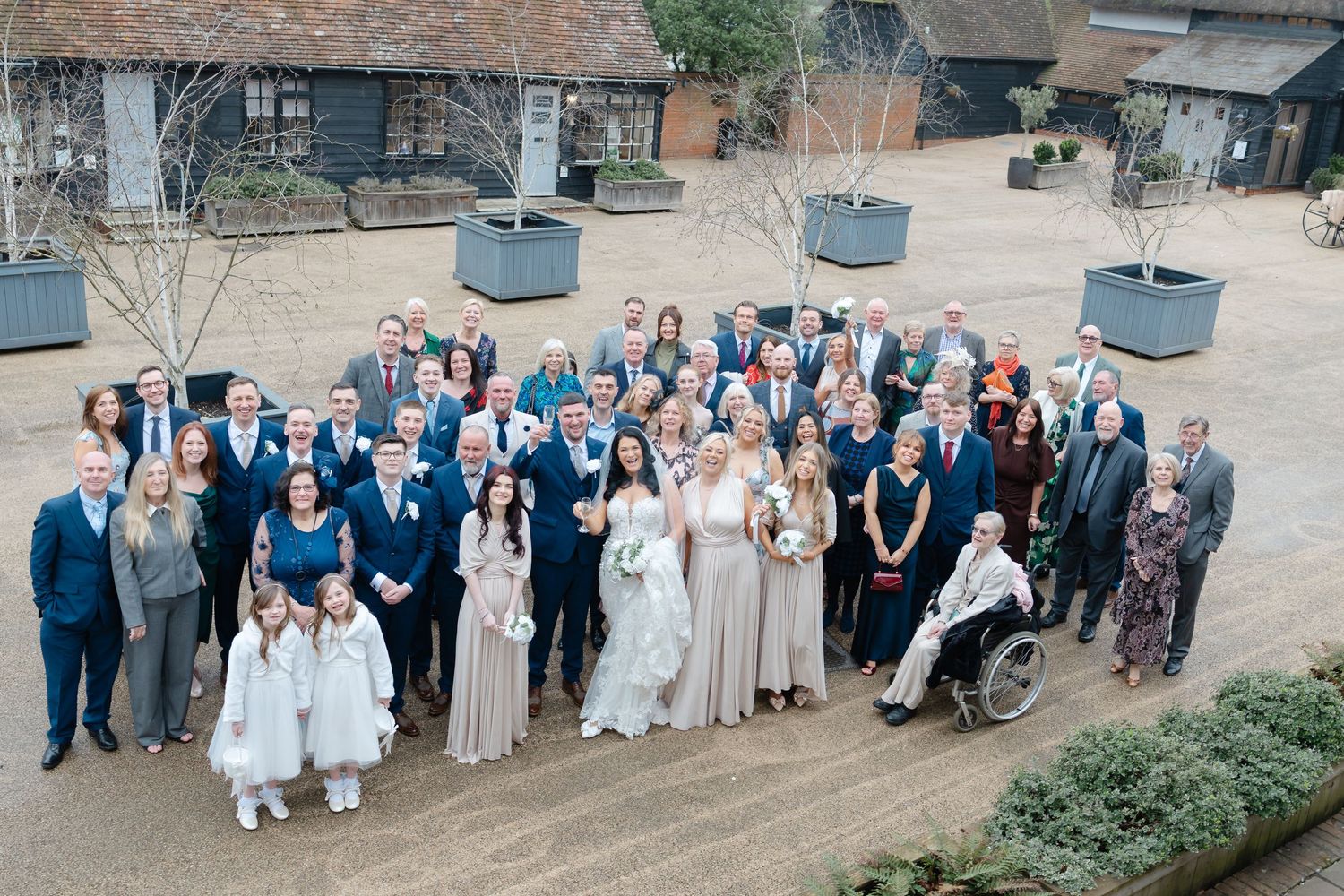 Large wedding party group photo with guests in navy and neutral colors against an outdoor backdrop.