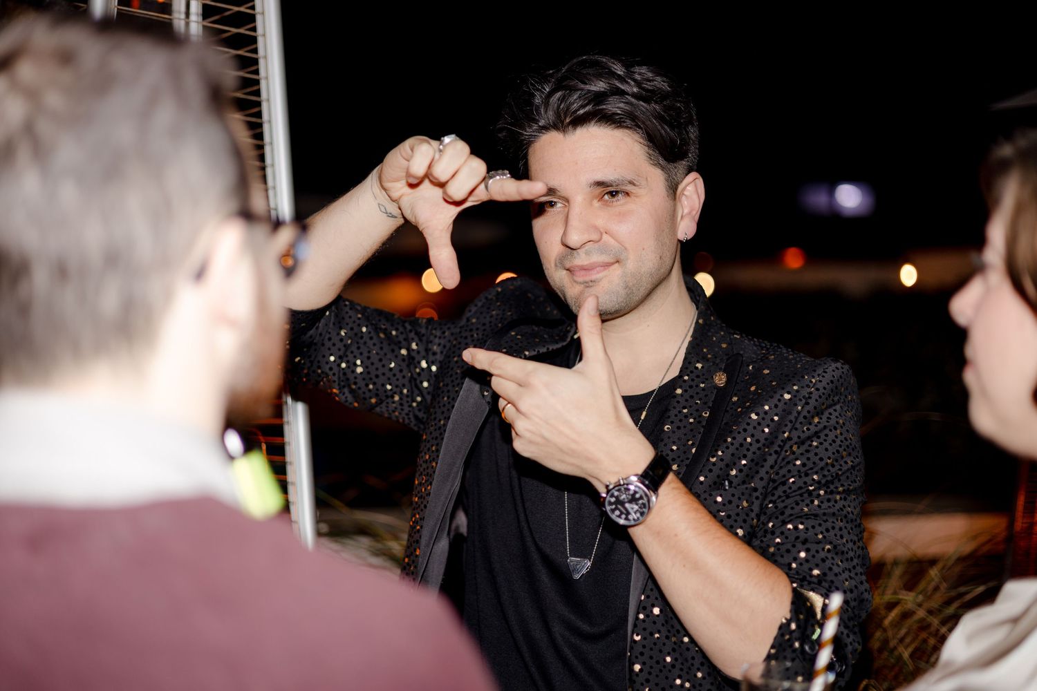 Person in a sparkly black shirt making playful hand gestures at a social event.