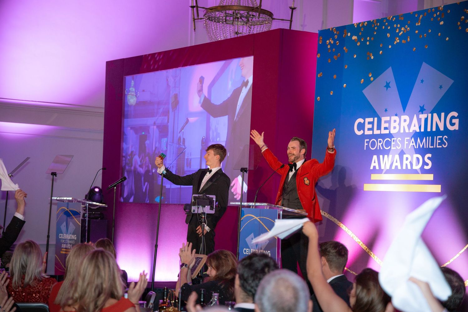 Performers on stage at an awards ceremony with colorful lighting and celebration banner.
